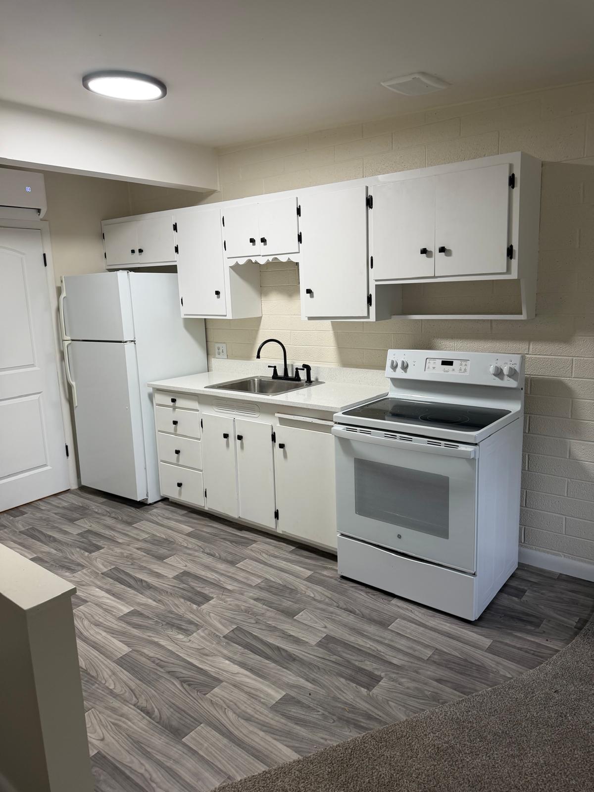 Kitchenette with white cabinetry, wood-finish flooring, white appliances, and a black gooseneck faucet