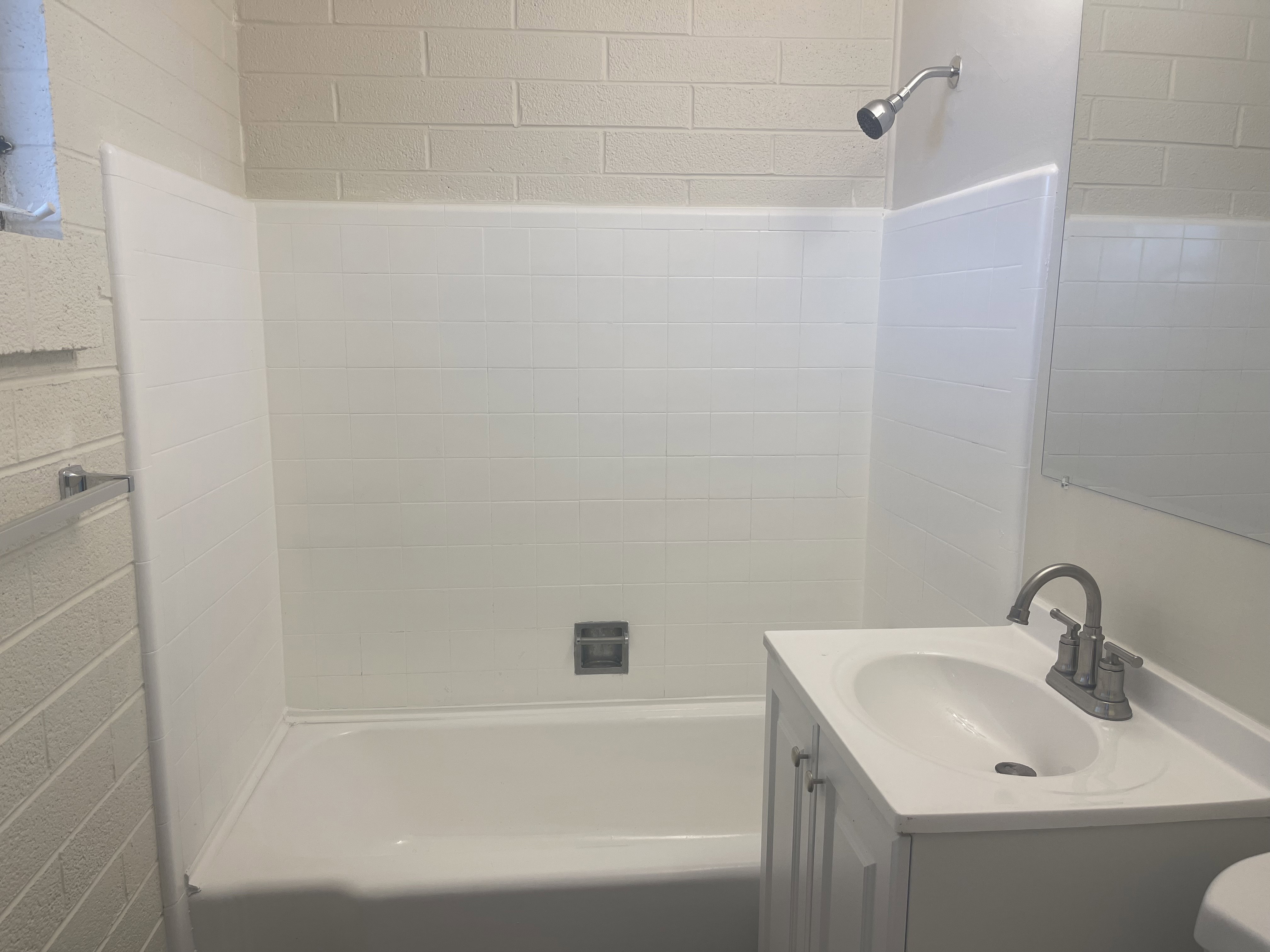 Bathroom featuring a white bathtub, white tiled shower surround, a chrome showerhead, a white vanity with an integrated sink, and a chrome faucet