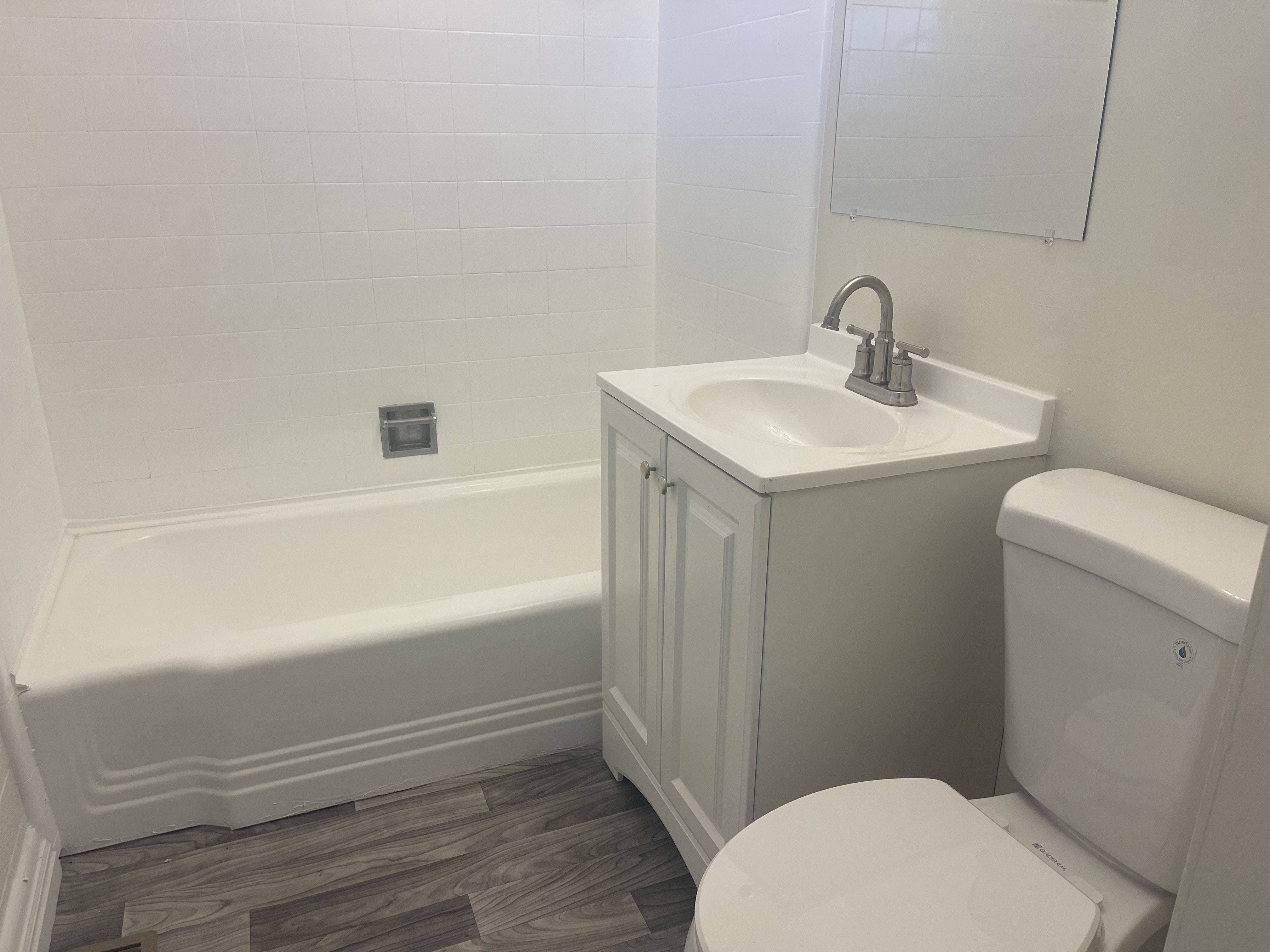 Bathroom featuring white subway tile surround, white bathtub, white vanity with integrated sink, and wood-finish flooring