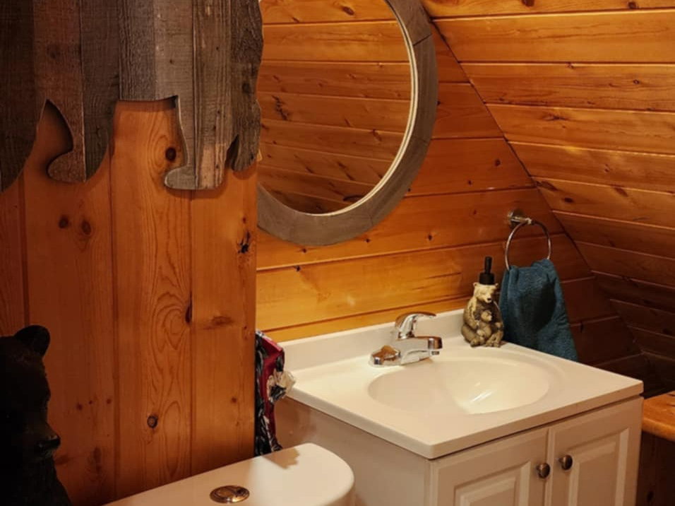 Wood-paneled room featuring a white single-vanity cabinet with an integrated sink, a circular framed mirror, and a white toilet