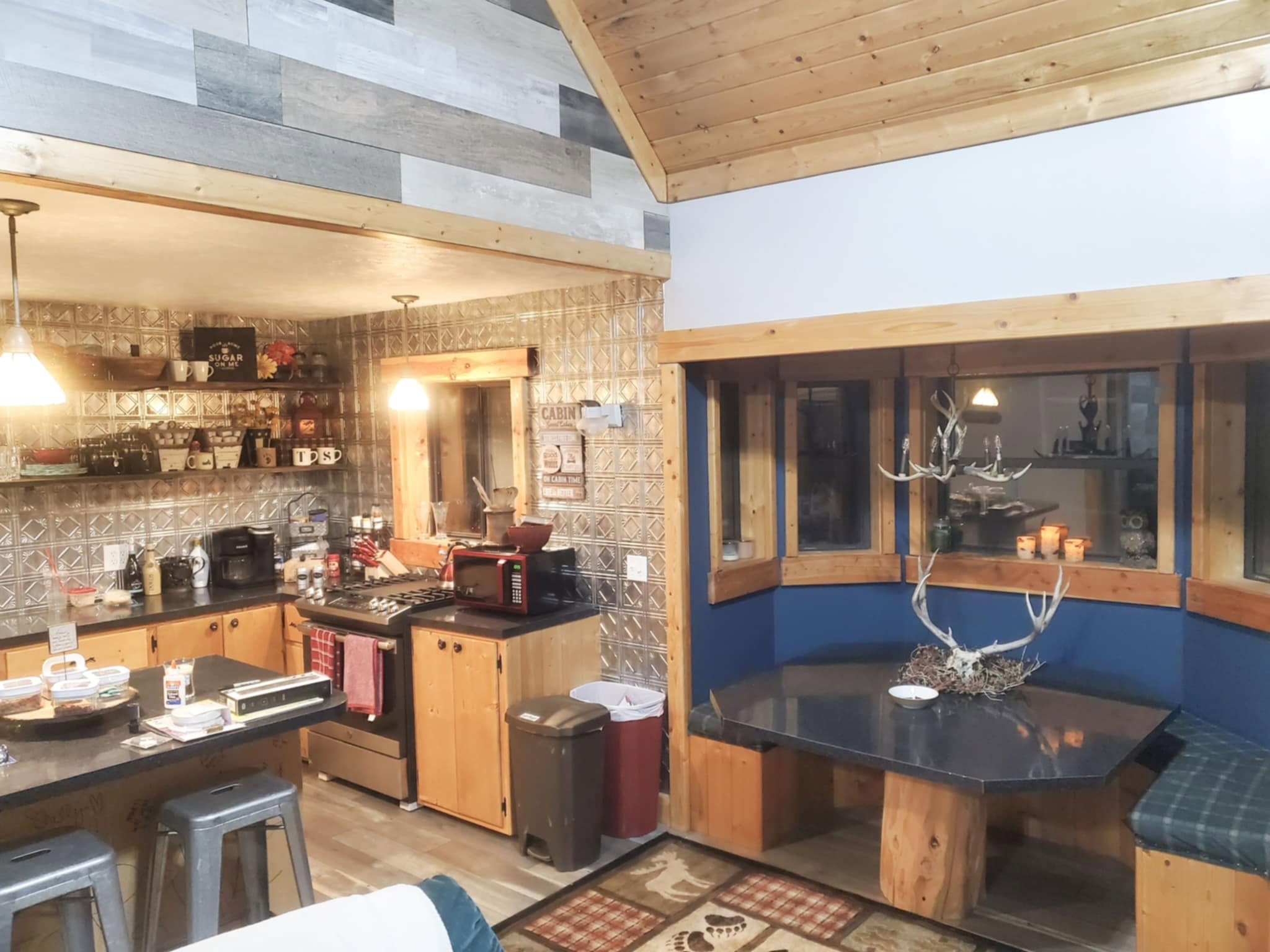 Open-concept kitchen and dining area featuring a tile backsplash, wood-finish flooring, a built-in dining nook with bench seating, and wood-paneled accents