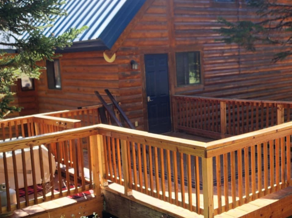 Wood-sided chalet-style residence featuring a metal roof, an expansive multi-level wood deck, and surrounding mature trees