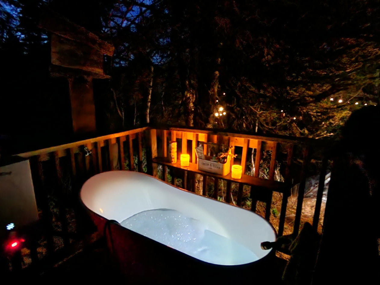 Outdoor deck featuring a freestanding bathtub, wood railing, and a built-in shelf