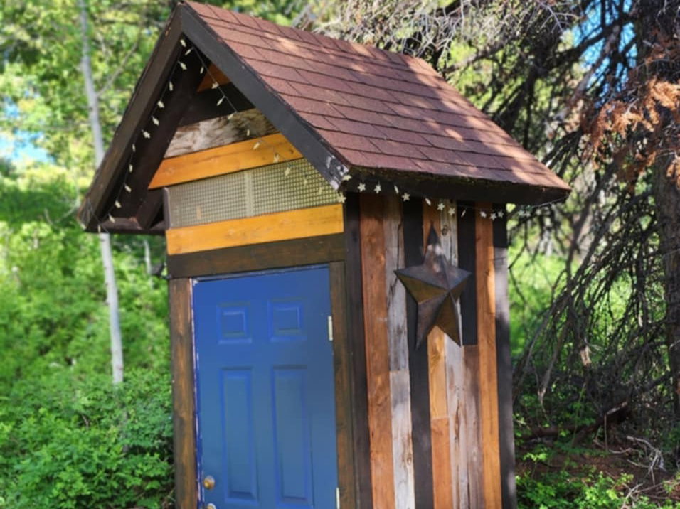 Wood-sided outbuilding featuring a pitched roof with shingles, a blue paneled door, and a decorative star accent