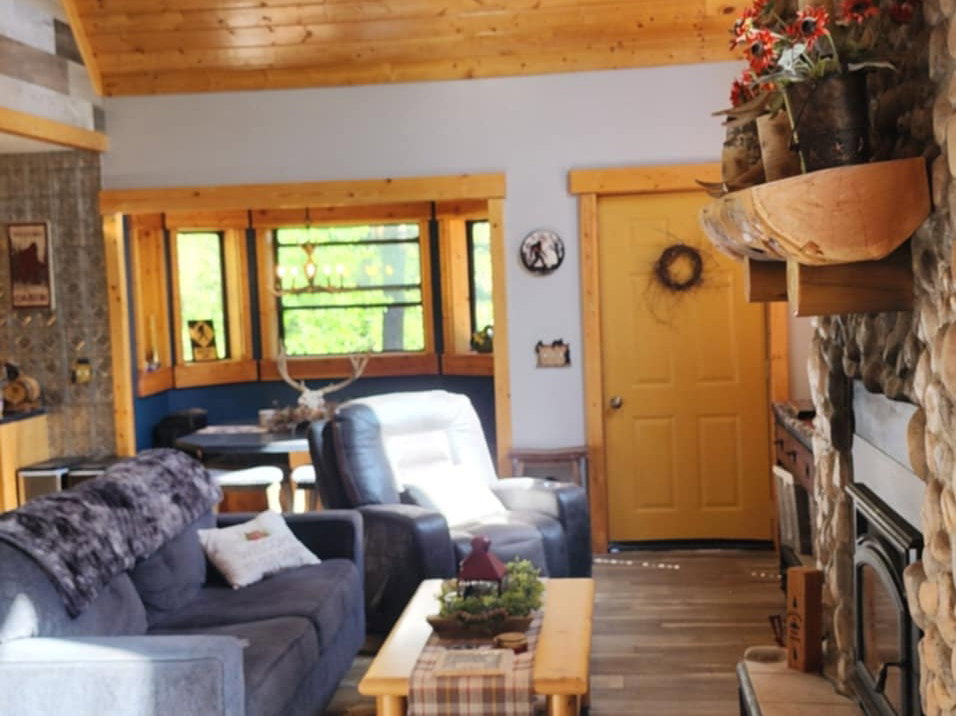 Living area featuring a vaulted wood-paneled ceiling, a stone fireplace, wood-finish flooring, and recessed windows with wood trim