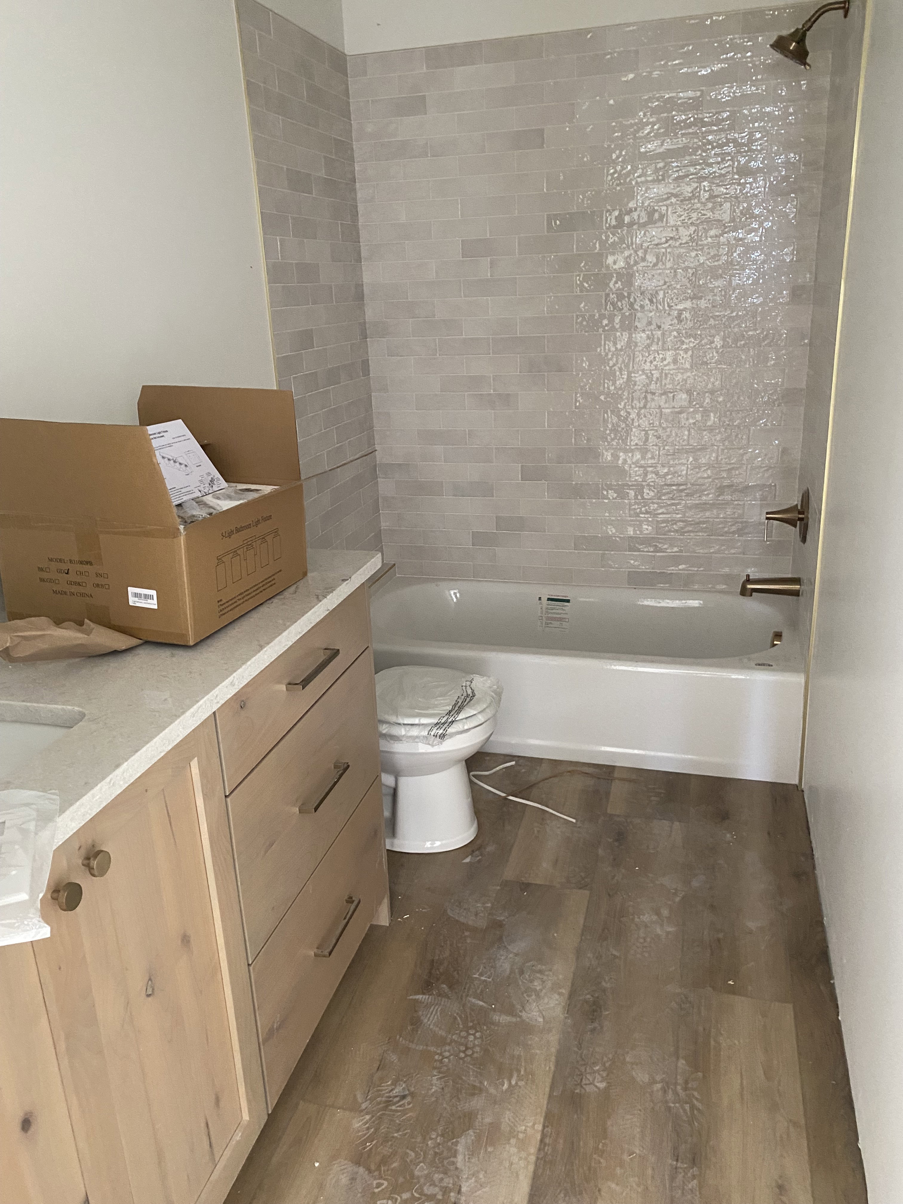 Bathroom featuring wood-finish flooring, a white bathtub with light gray subway tile surround, and bronze fixtures