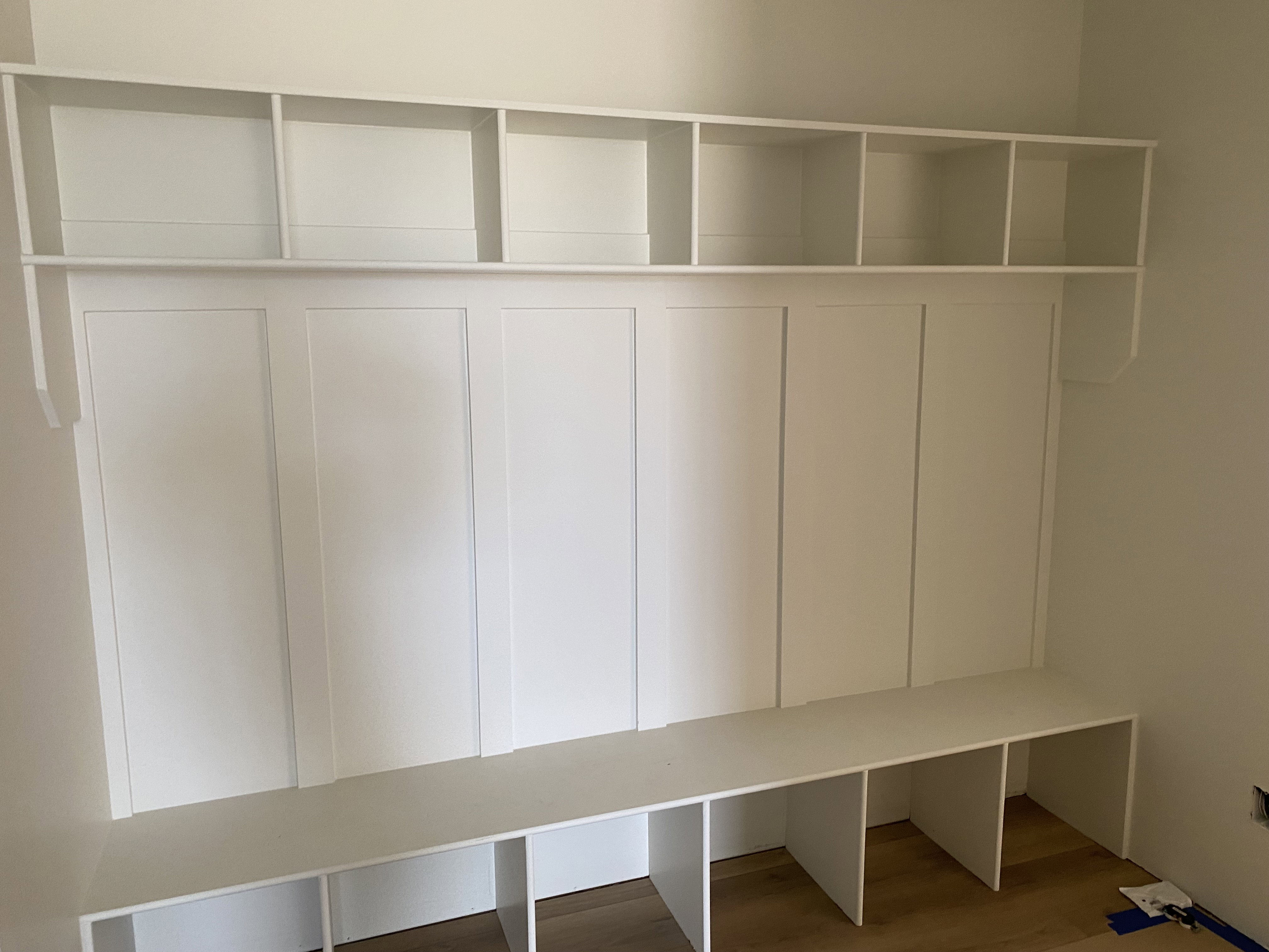 Built-in white storage bench with open shelving, wall paneling, and wood-finish flooring