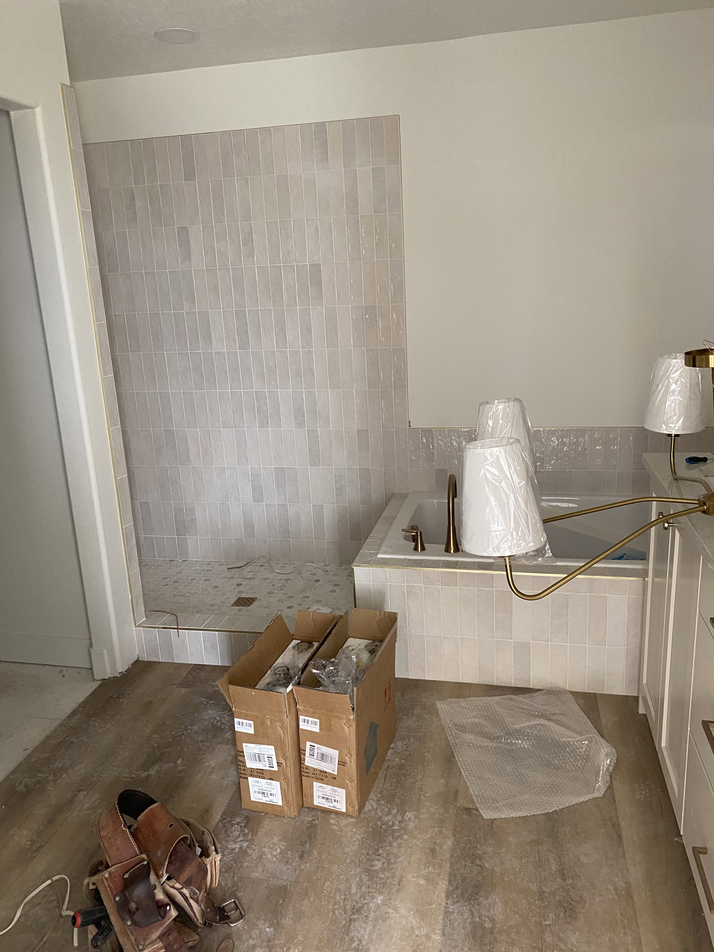 Bathroom featuring a walk-in shower with vertical subway tile, a built-in tub with coordinating tile surround, and an adjacent vanity with white cabinetry and gold-tone hardware