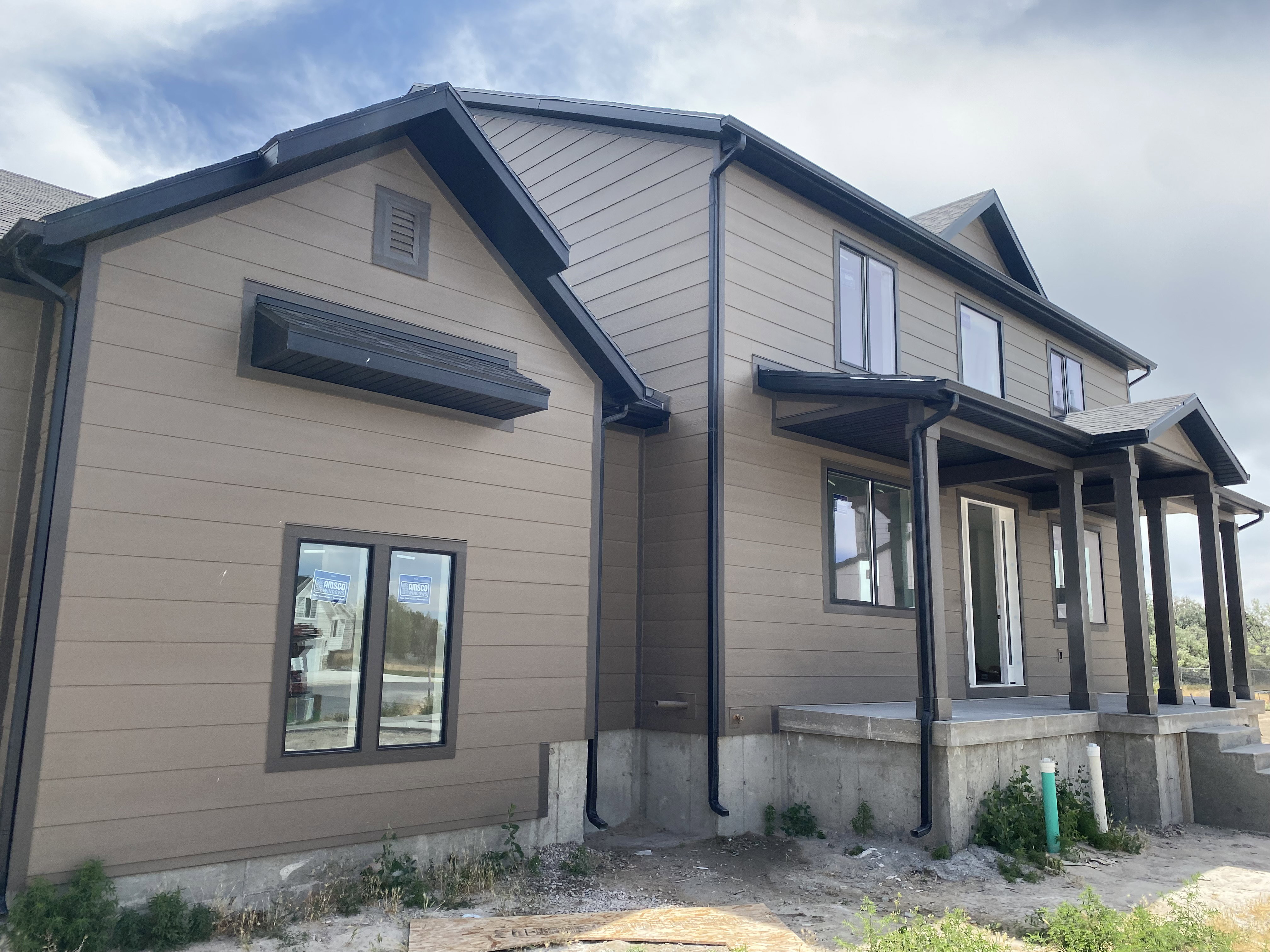 Exterior featuring horizontal siding with dark trim, multiple windows with dark frames, a covered front porch with dark columns, and dark-finished gutters