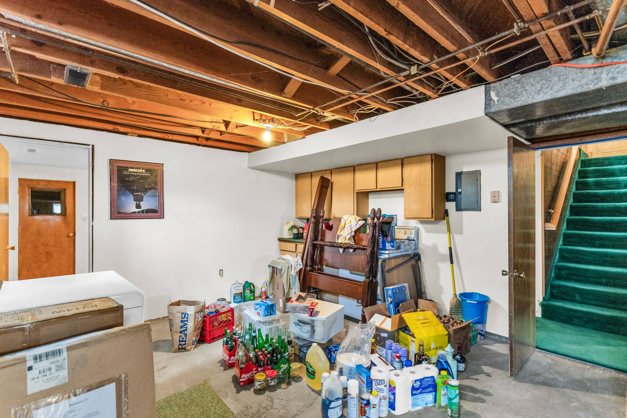 Basement utility area featuring exposed wood joists, partial finished walls, and a green carpeted staircase with wood railing