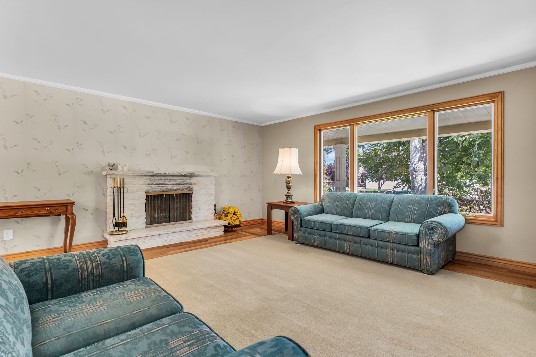 Living area featuring a brick fireplace, wood-finish flooring, a neutral carpet, and large windows with wood trim