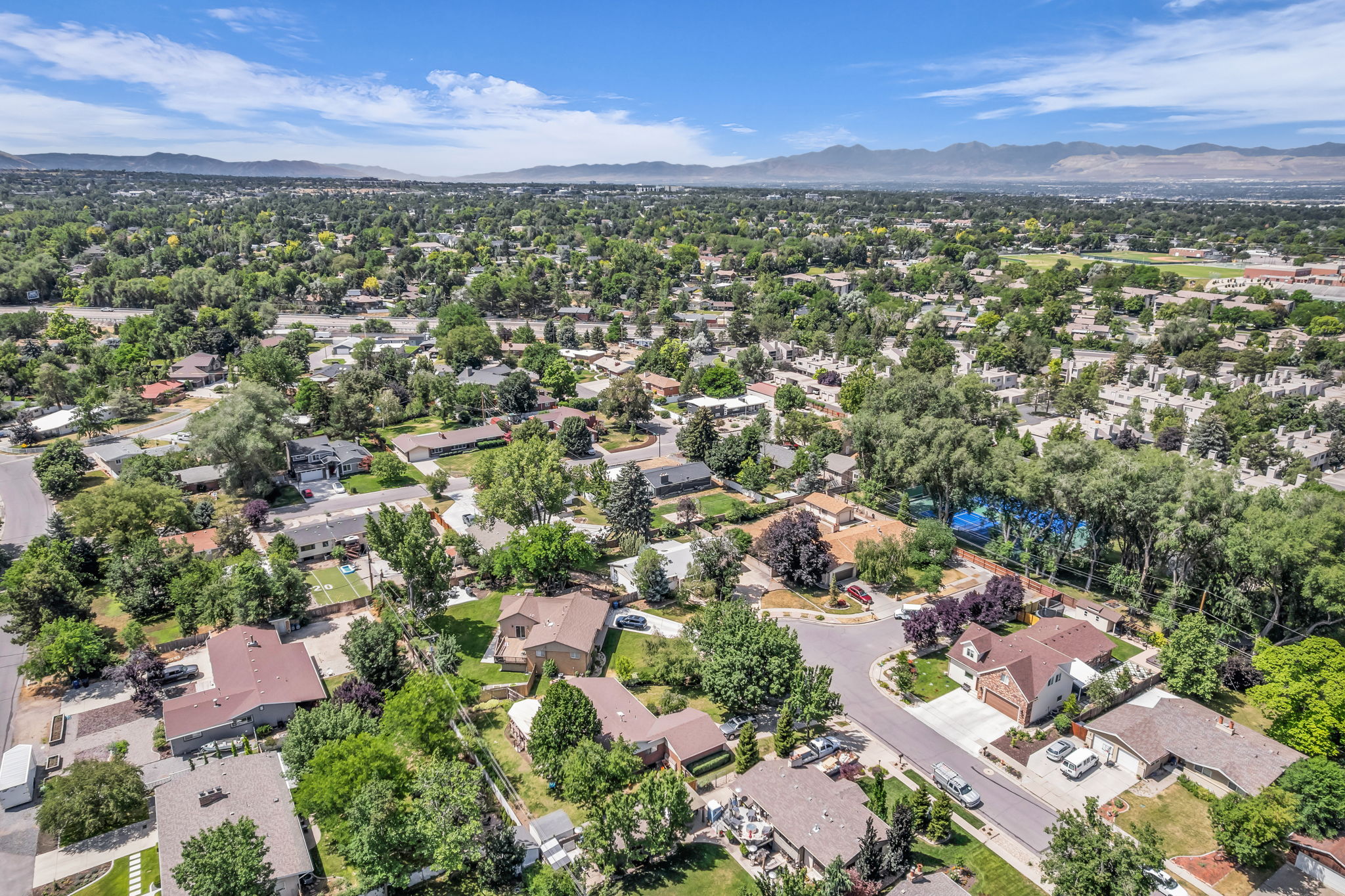 Aerial perspective showcasing a residential neighborhood with abundant mature trees and mountain scenery