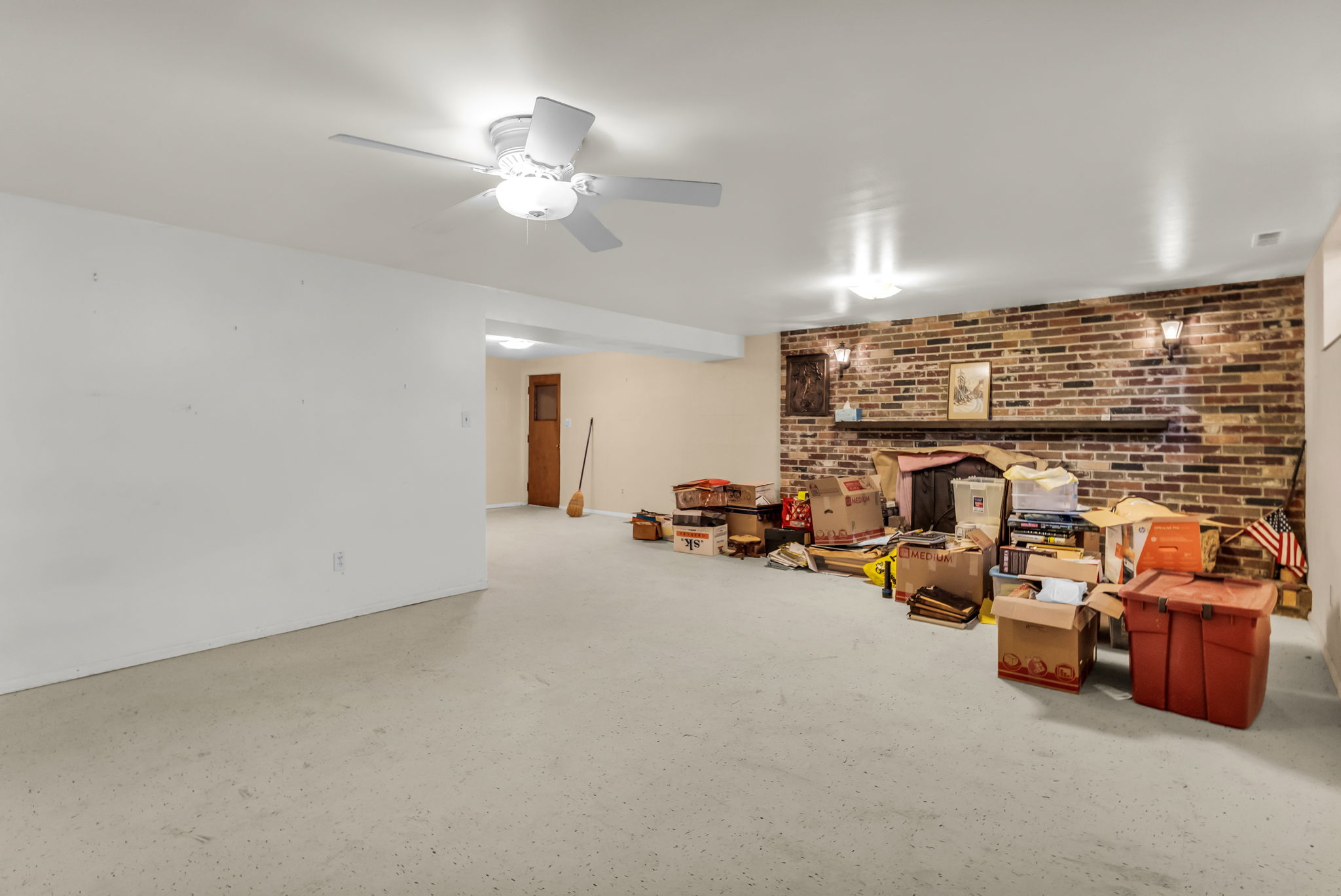 Spacious interior room featuring a decorative brick wall with a built-in mantel, overhead lighting, and a ceiling fan