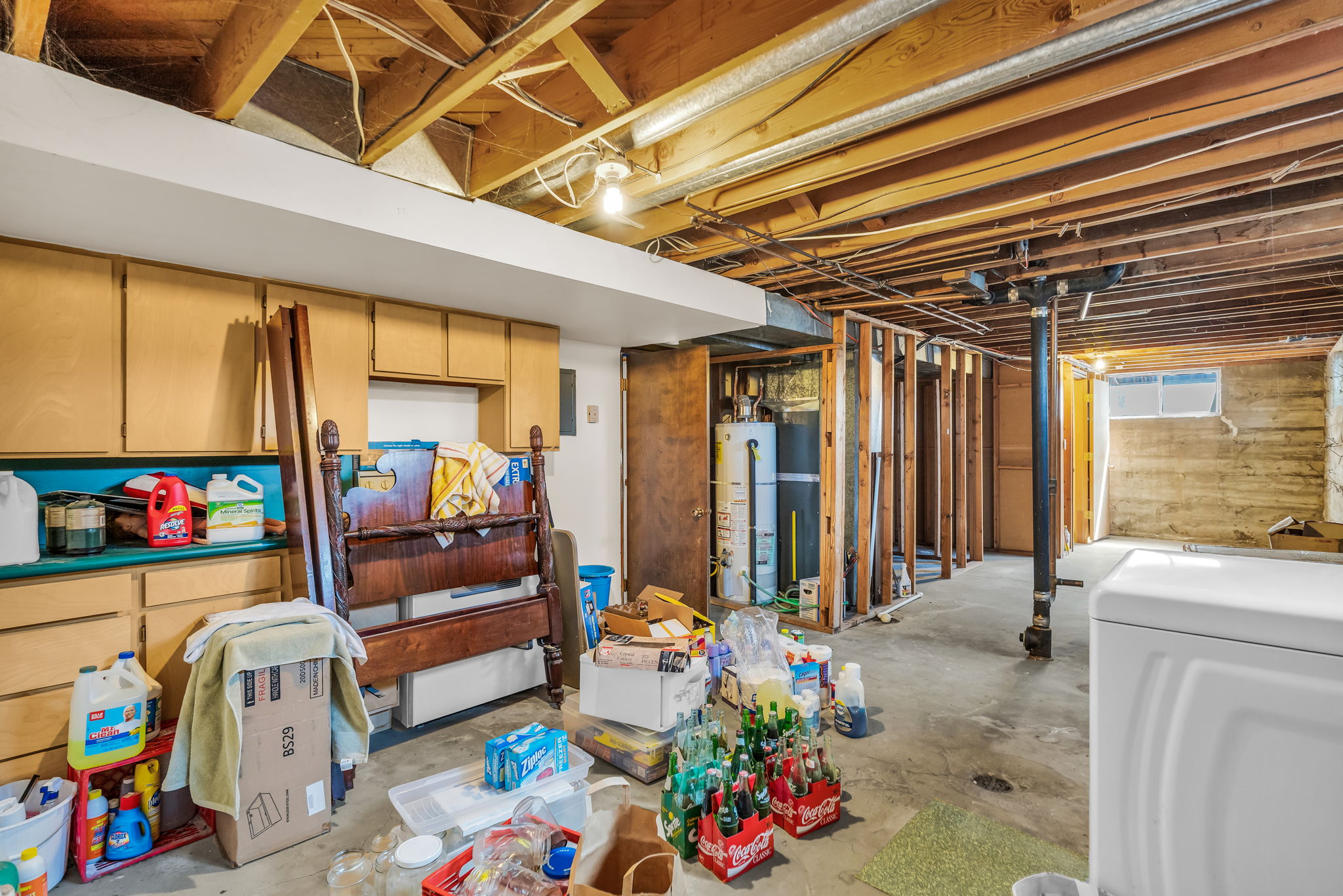 Unfinished basement featuring exposed wood joists, concrete flooring, built-in cabinetry with a countertop, and a visible water heater