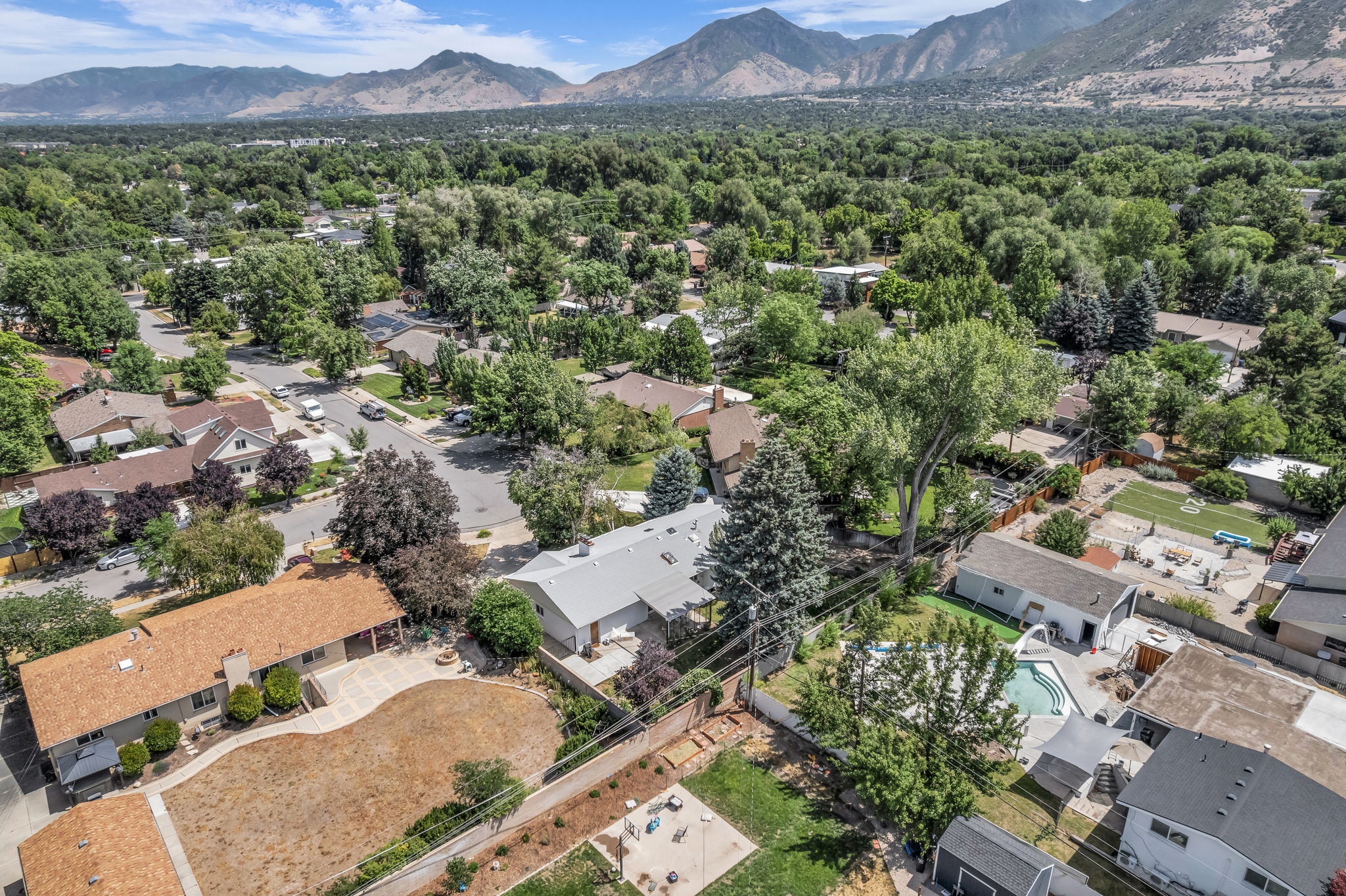 Aerial property view showcasing a residential neighborhood with mature trees and mountain scenery