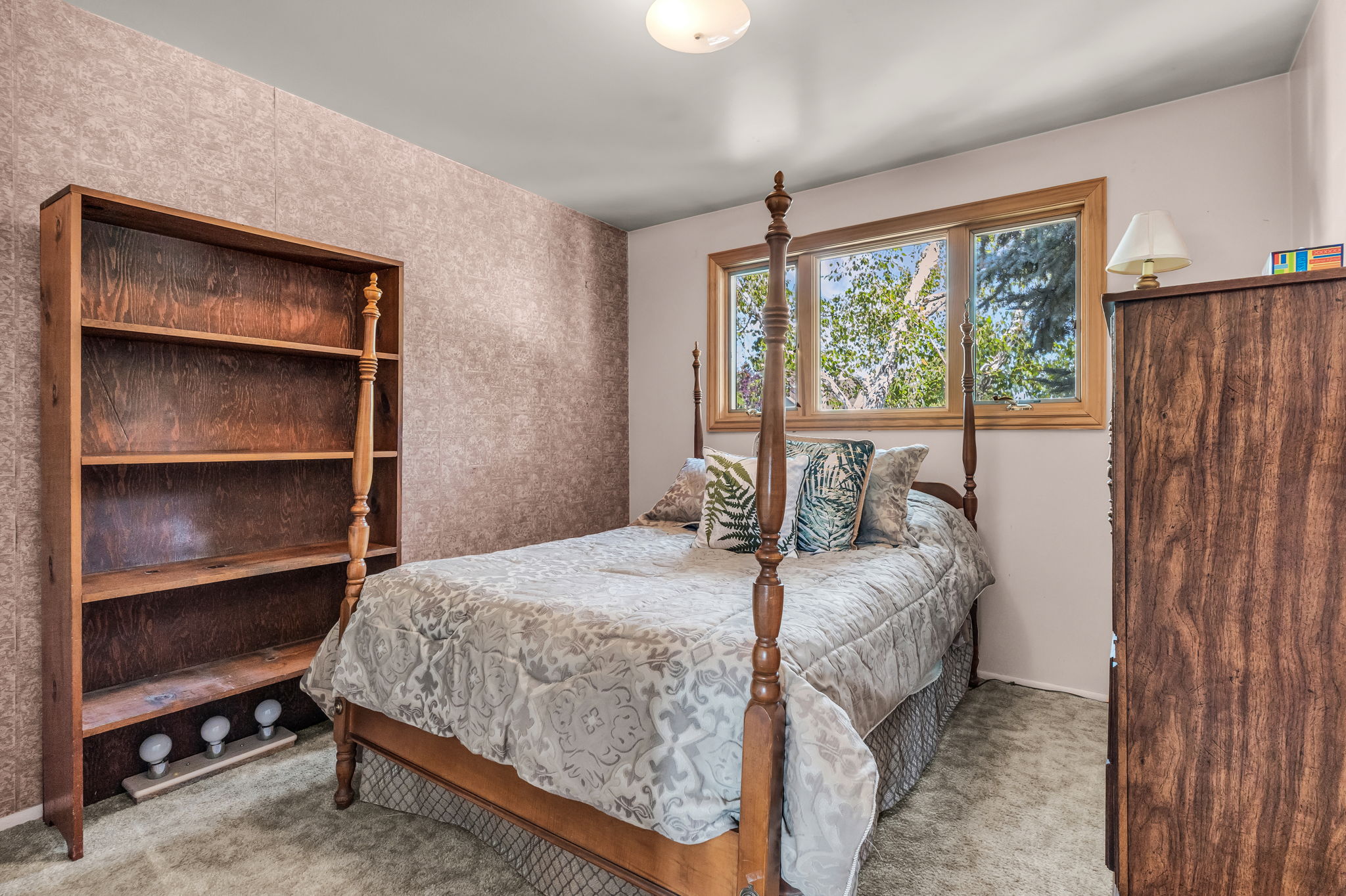 Room featuring a triple window with wood-finish trim, textured wall covering, and neutral carpeting