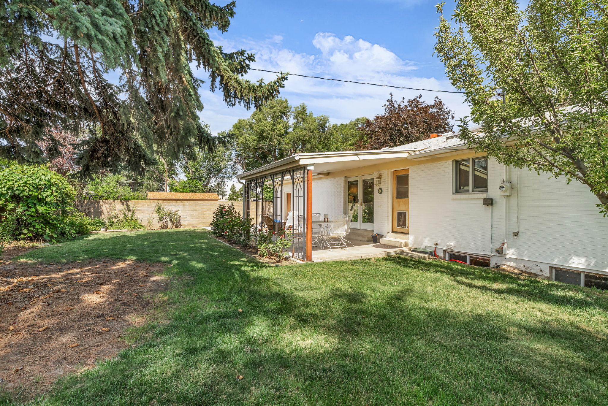Expansive backyard featuring a covered patio, mature trees, and a white brick exterior