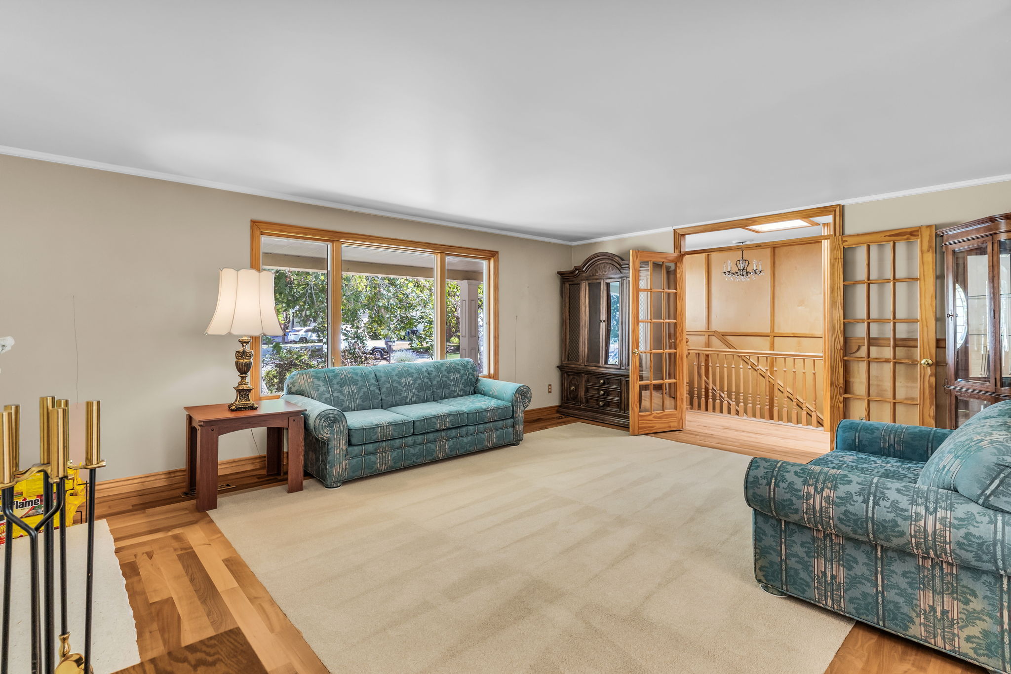 Living area featuring a large window with wood trim, light-toned carpeting, and wood-finish flooring
