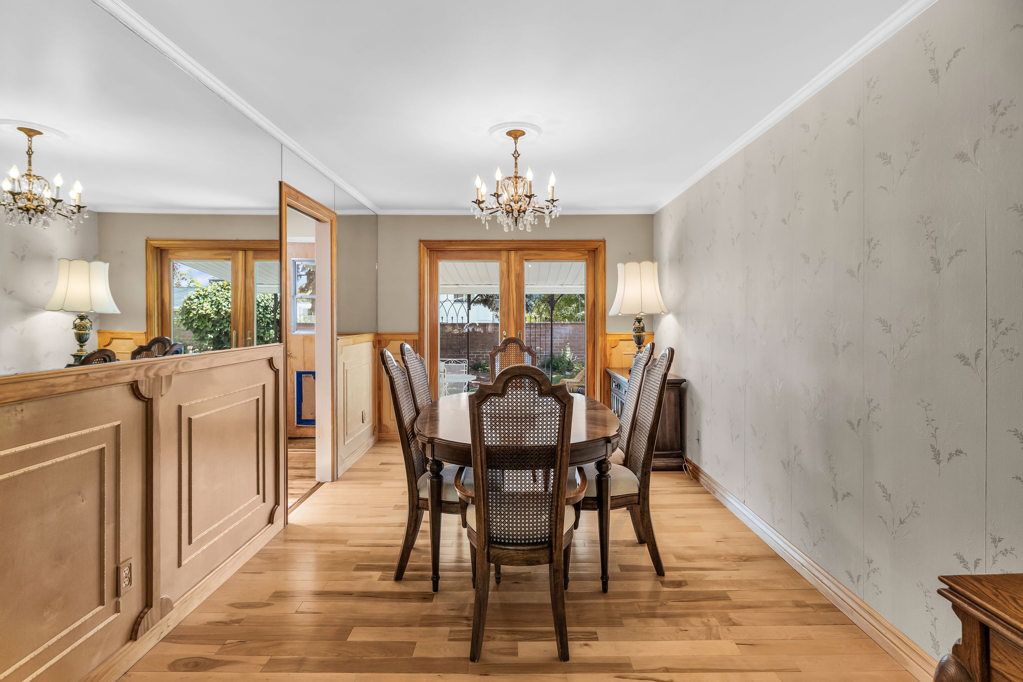 Dining area featuring wood-finish flooring, two chandeliers, wainscoting, decorative wallpaper, and natural light from exterior doors