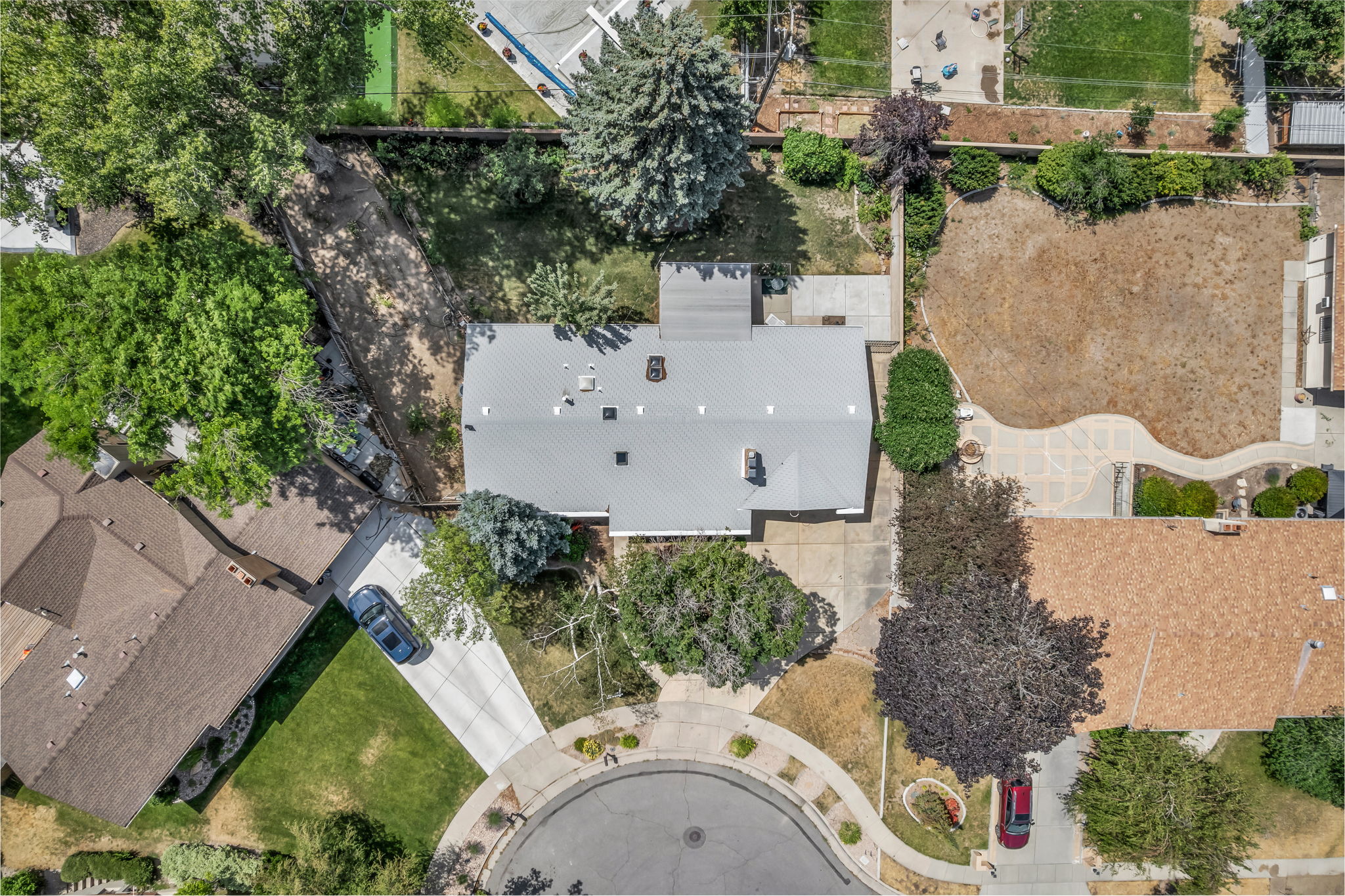 Property featuring a light gray roof, mature trees, and a concrete driveway