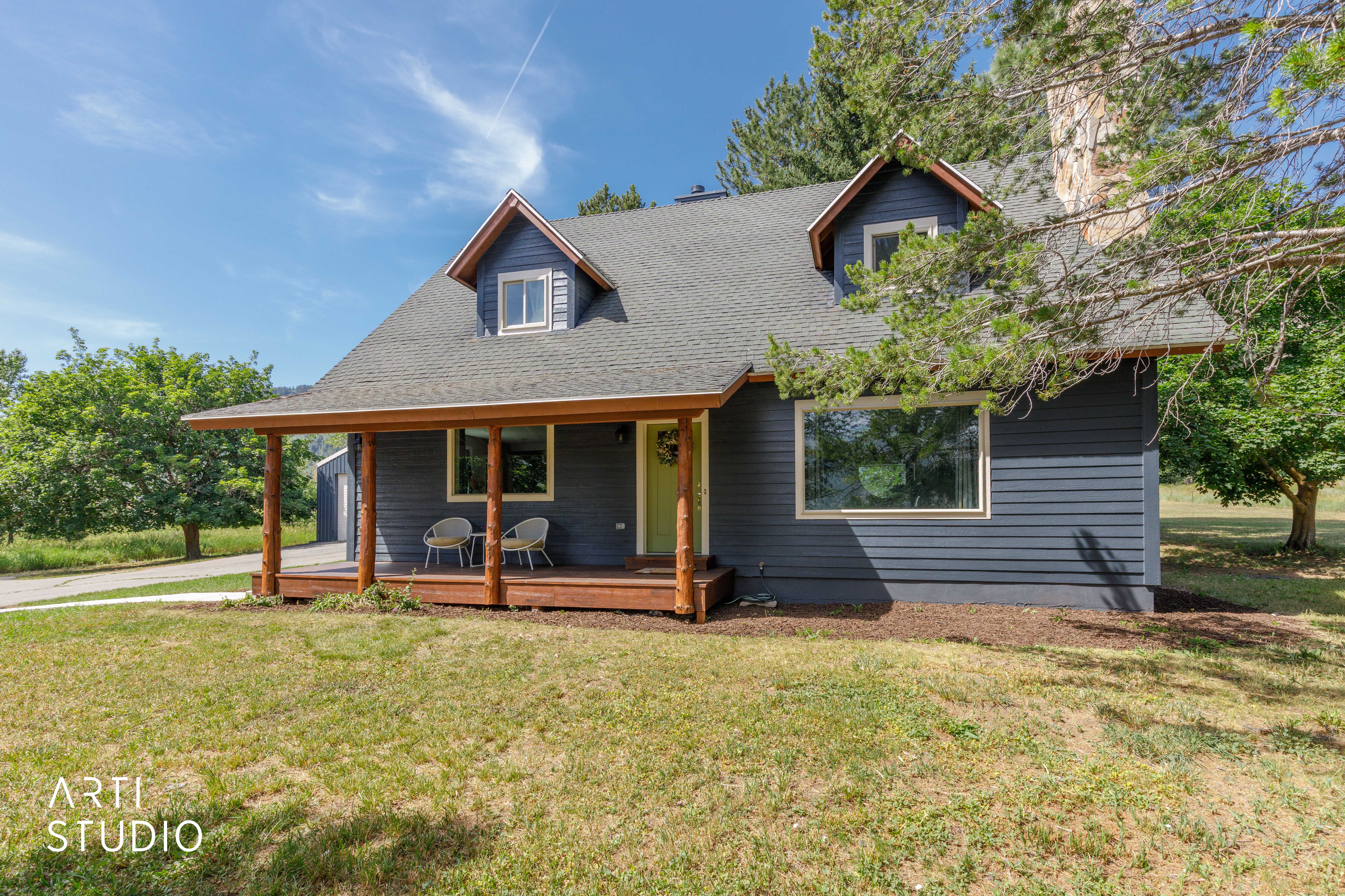 Exterior featuring a spacious covered porch with natural wood posts, dark siding, dormer windows, a light-colored front door, and a shingle roof