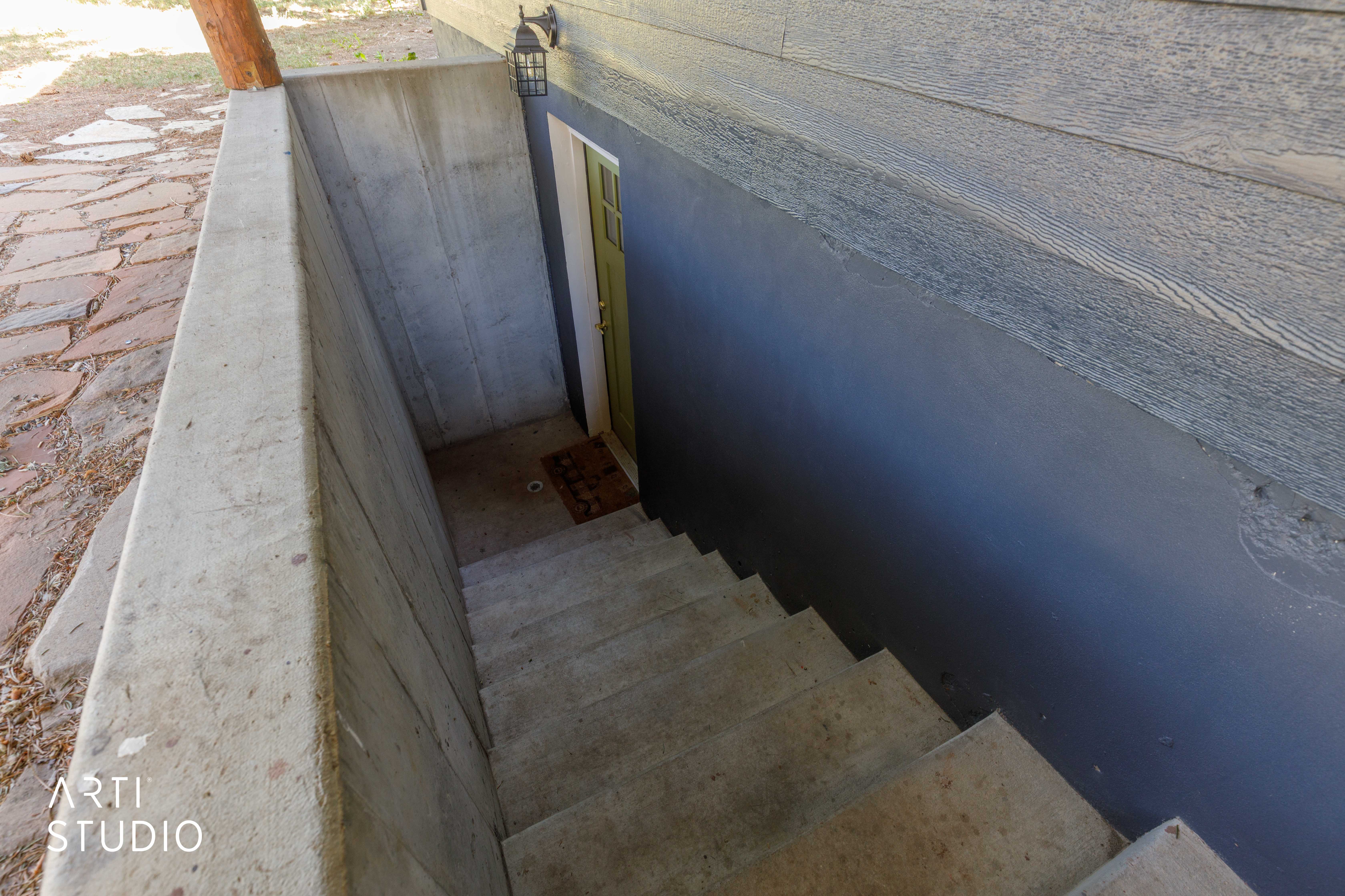 Separate entry for basement. Concrete outdoor stairs descending to a recessed entry with a green door