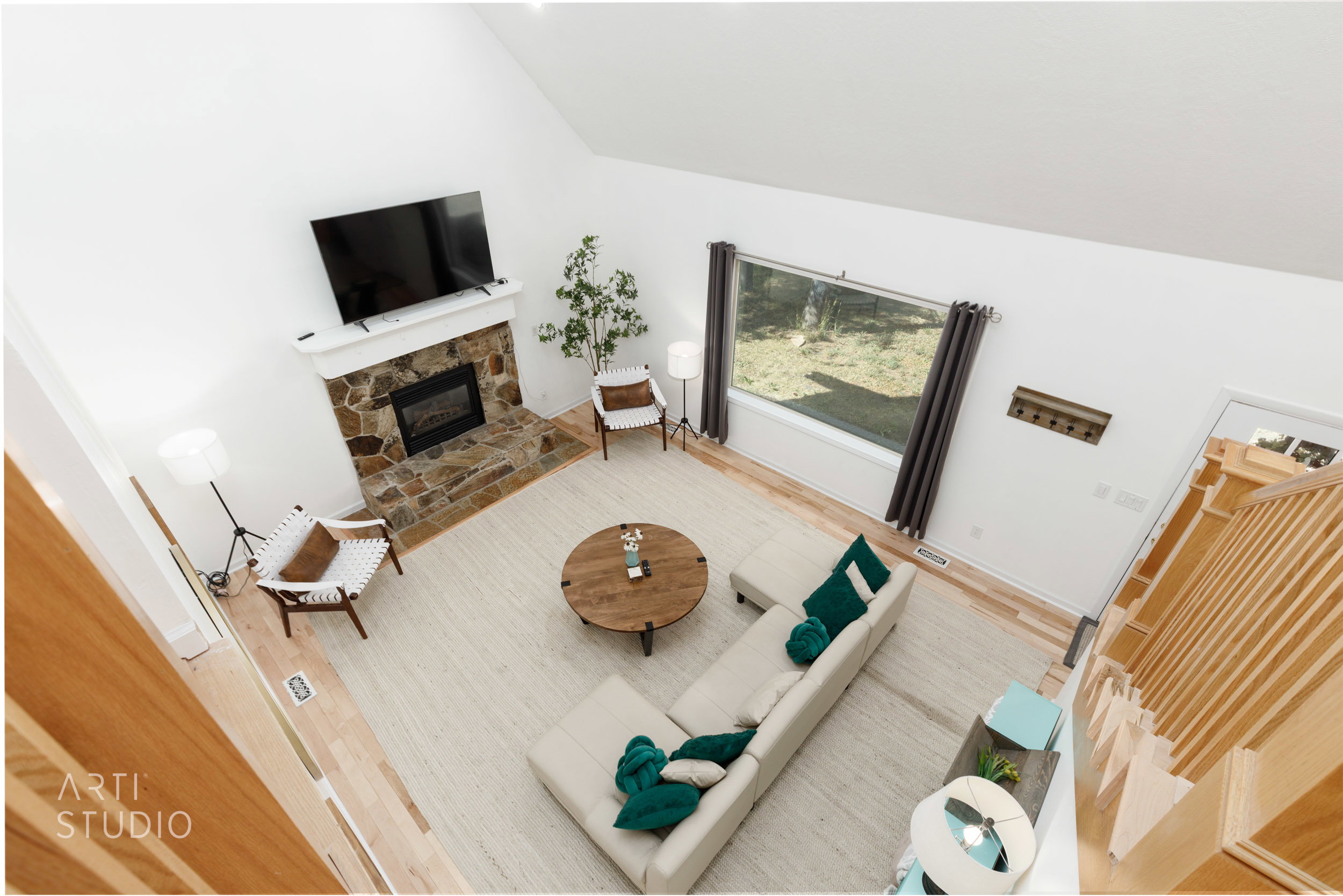Expansive living area featuring a vaulted ceiling, stone fireplace with a white mantel, wide window, light wood-finish flooring, and a natural wood staircase