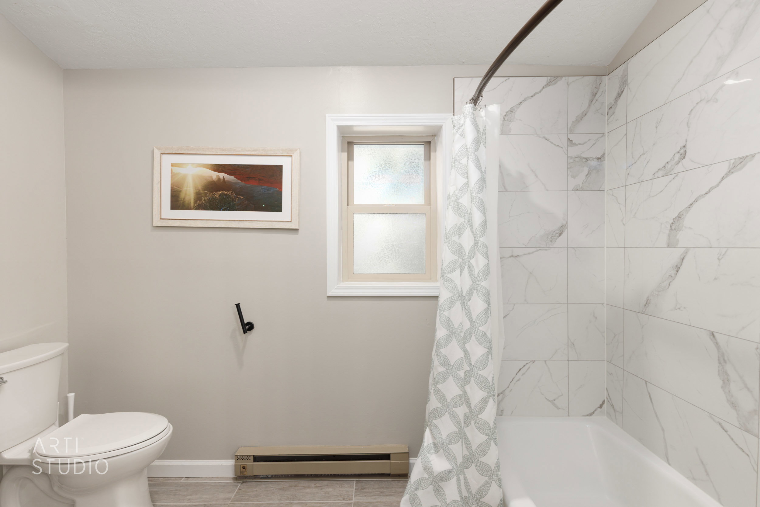 Bathroom featuring a white porcelain toilet, white window trim, white subway tile shower surround with gray veining, and gray tile flooring