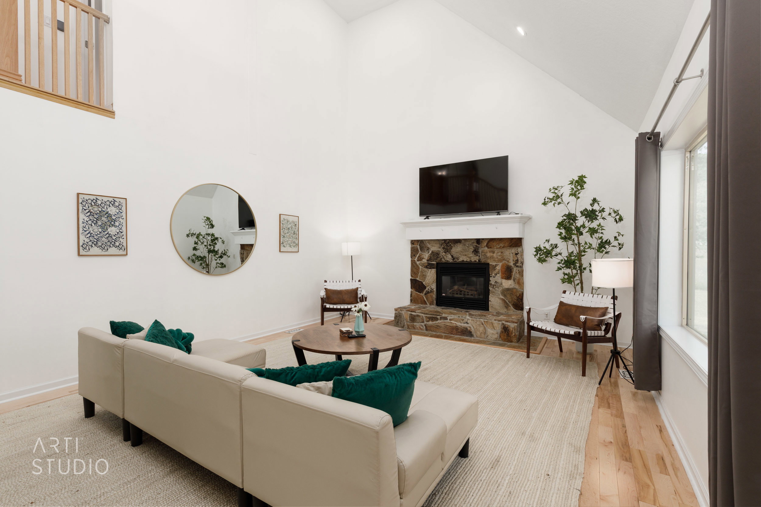 Vaulted ceiling living area featuring a stone-clad fireplace with a white mantel, wood-finish flooring, and a large window with dark drapes