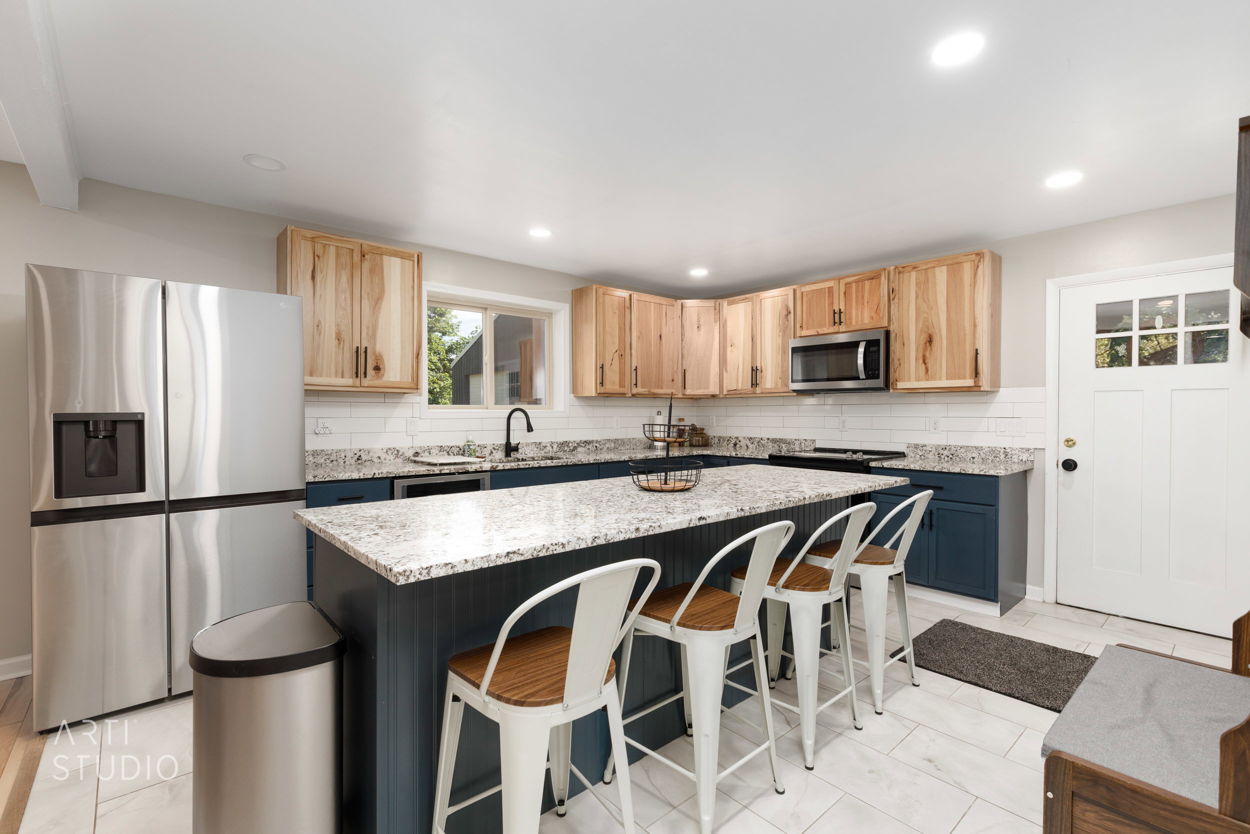 Kitchen featuring a large island with a granite countertop, shaker-style base cabinetry in a deep blue finish, natural wood-finish upper cabinetry, and a white subway tile backsplash