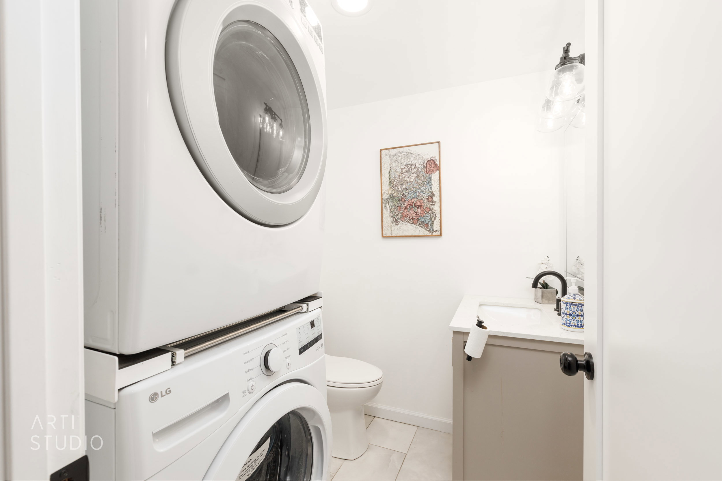 Stackable laundry appliances paired with a vanity featuring a white countertop and a black gooseneck faucet