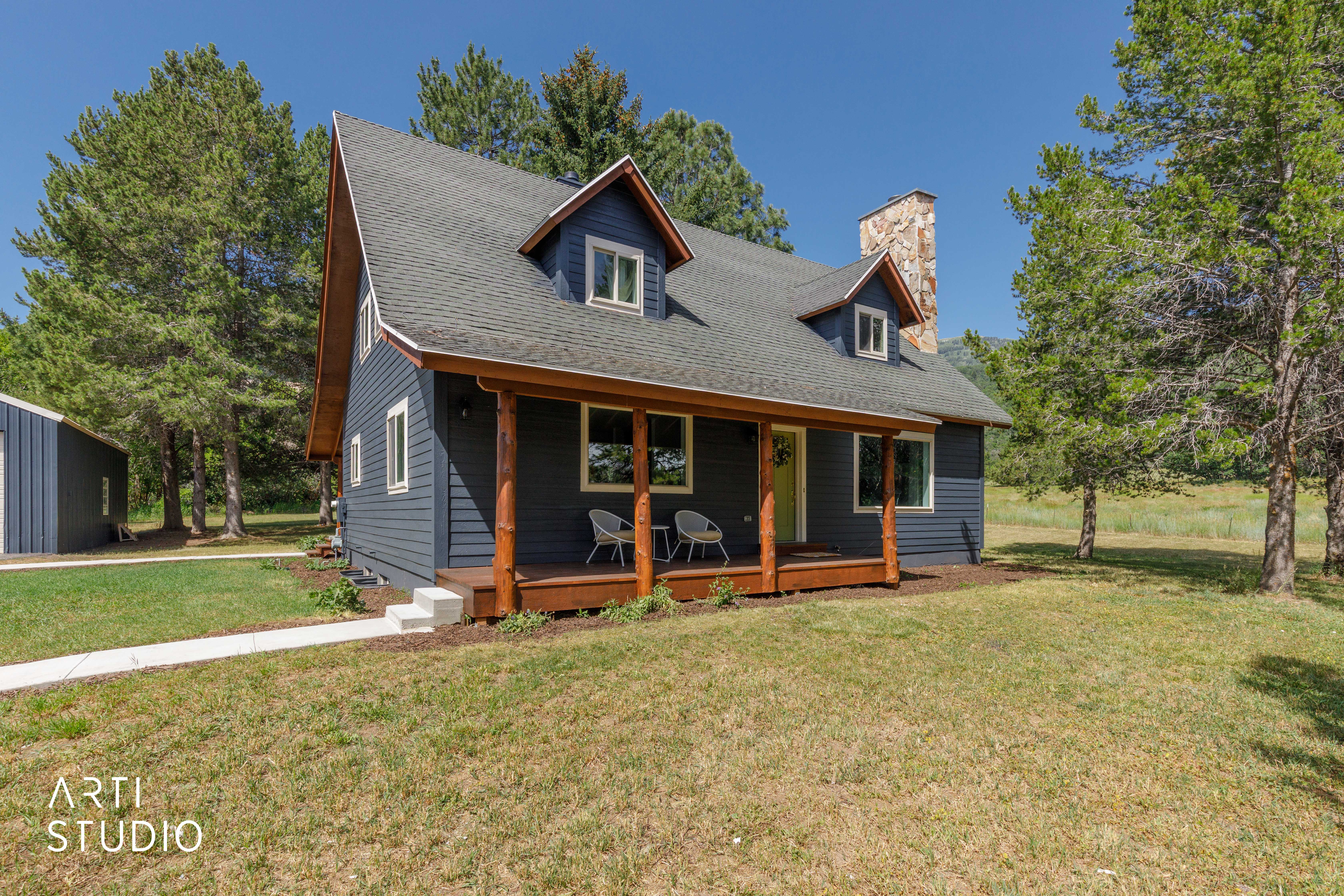 Charming residence featuring dark blue siding, a covered front porch with natural wood posts, and a prominent stone chimney