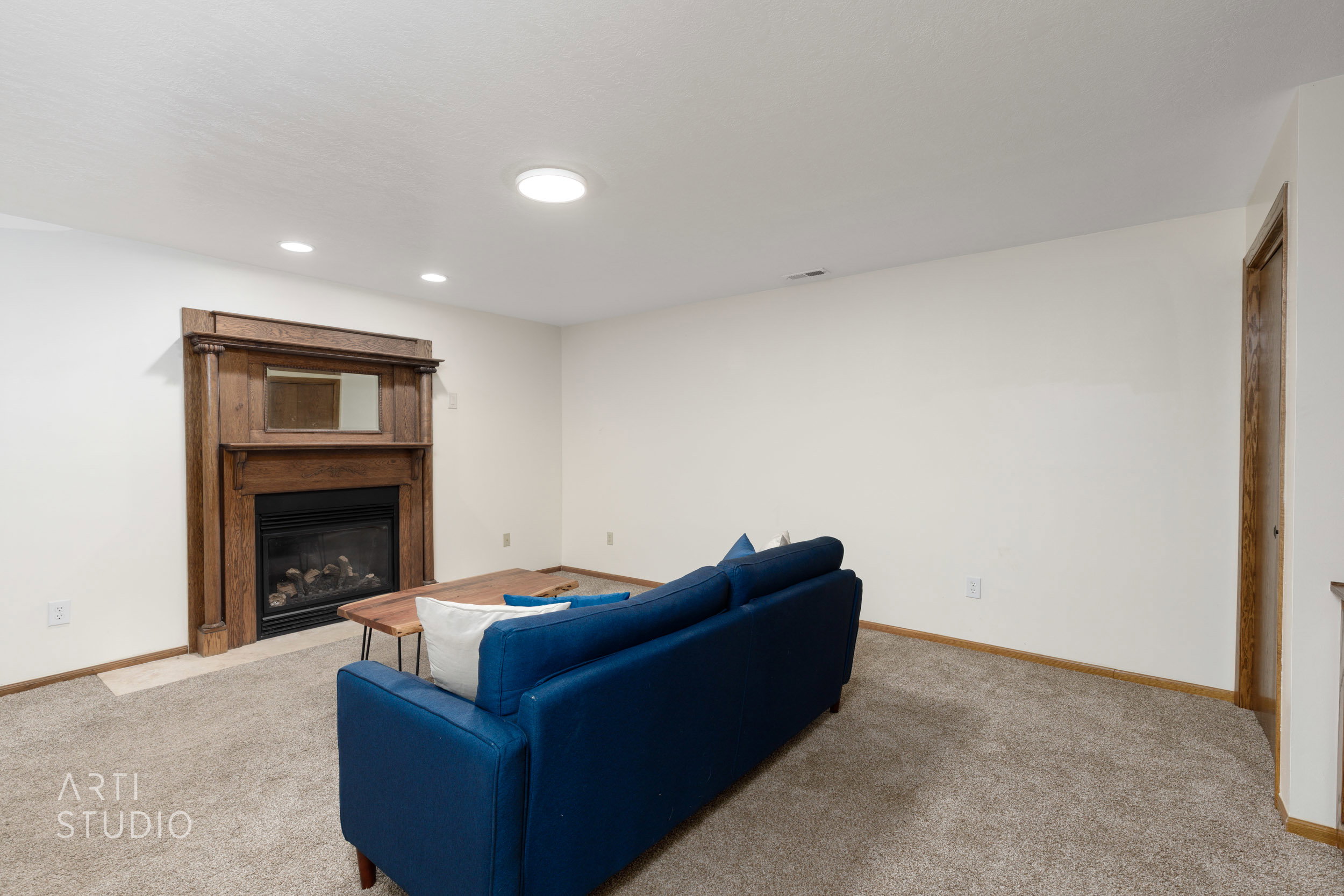 Living space featuring a detailed wood fireplace surround with an integrated mirror, recessed ceiling lighting, and neutral carpet flooring