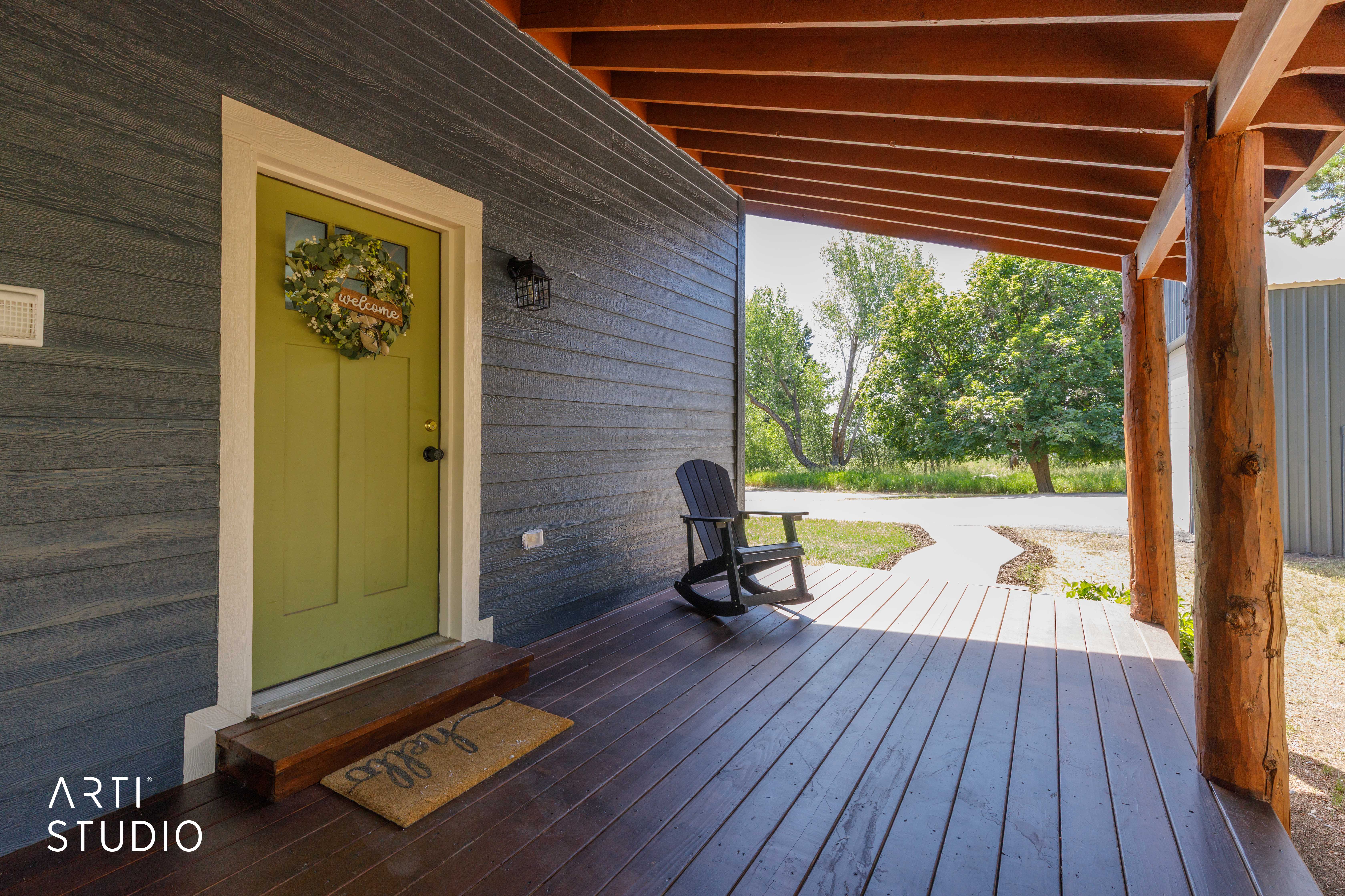 Covered porch featuring a vibrant green door with an overhead transom window, dark wood-finish decking, and exposed timber columns