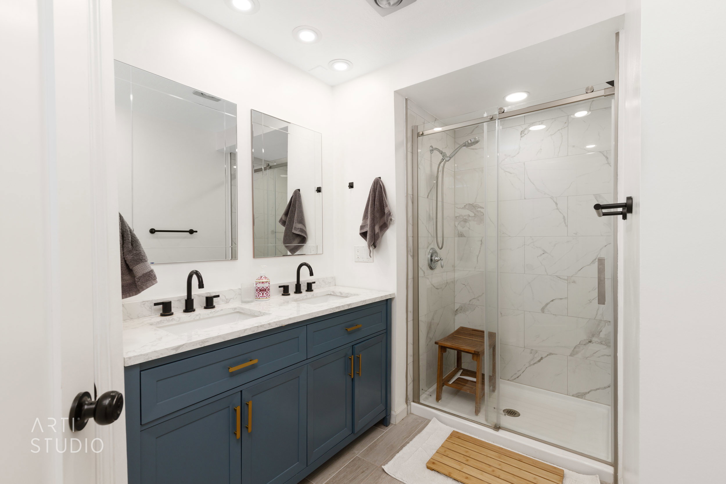 Bathroom featuring a dual vanity with a blue cabinetry and light-toned countertop, two framed mirrors, recessed lighting, and a glass-enclosed shower with tiled walls