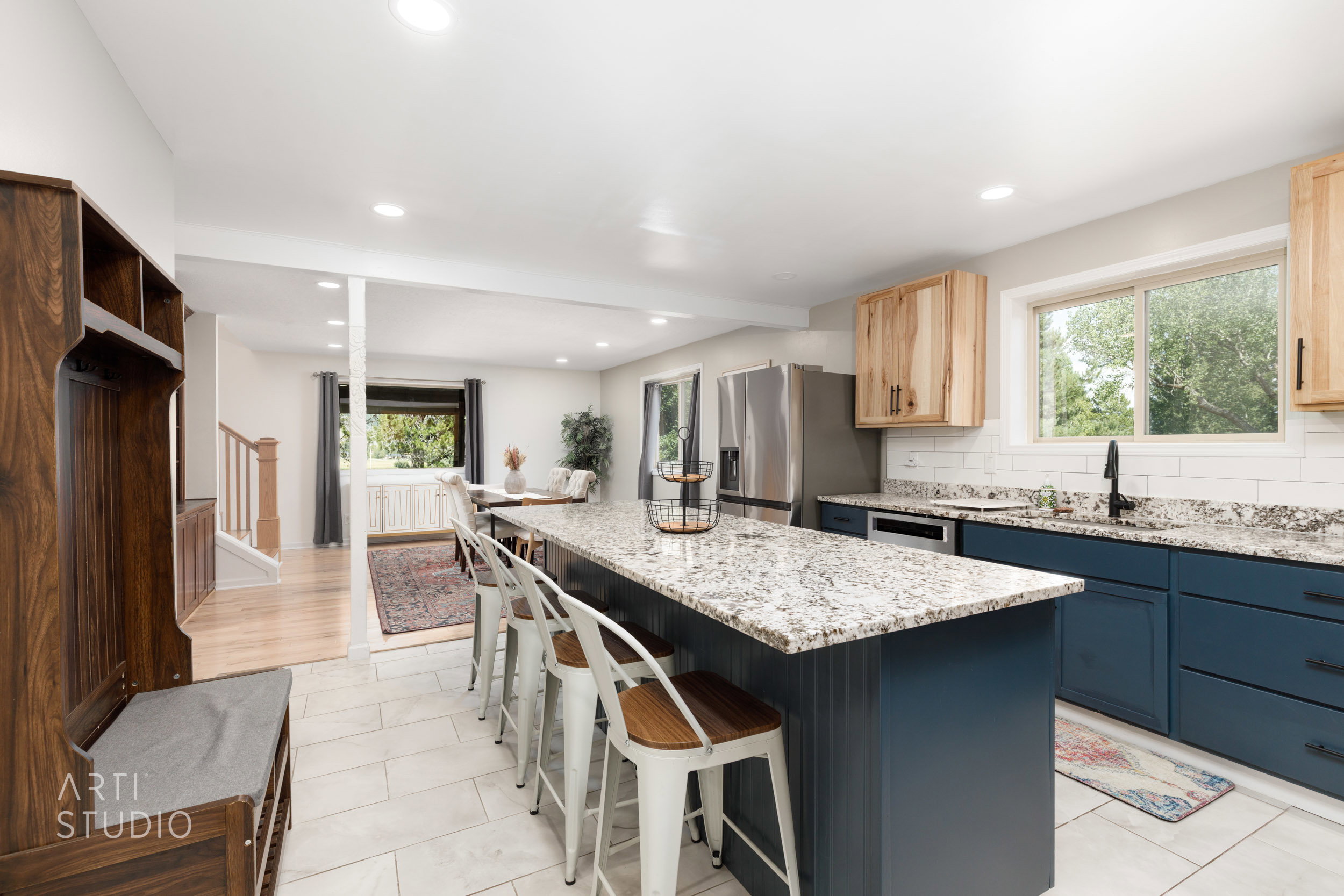 Bright kitchen featuring an expansive center island with granite countertops, blue shaker-style cabinetry, stainless steel appliances, and wood-finish flooring
