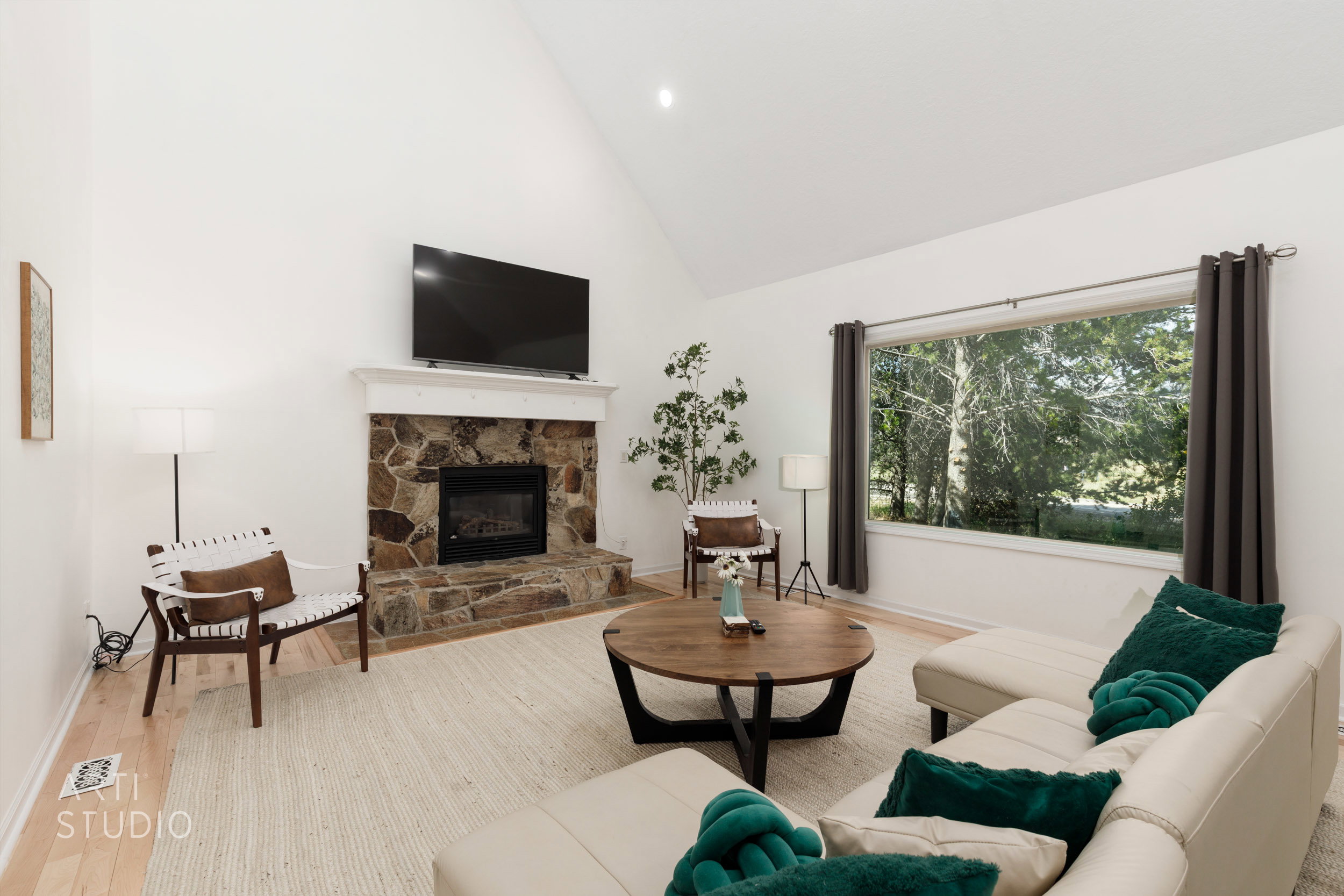 Vaulted ceiling living area featuring a stone-surround fireplace with hearth, a wood-finish floor, and a large picture window with outdoor scenery