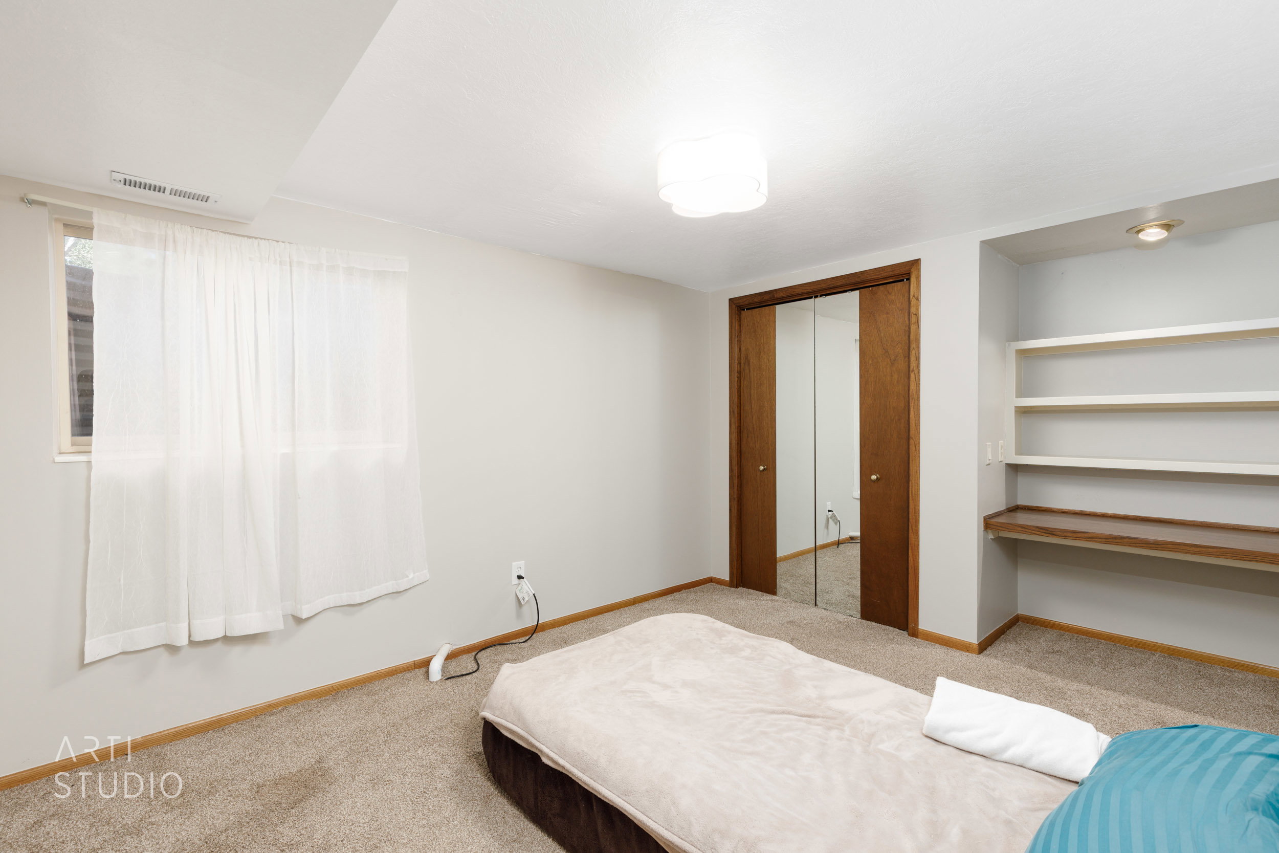 Carpeted room featuring a window, built-in shelving with an integrated desk surface, a mirrored closet with wood-finish sliding doors, and a flush-mount ceiling light fixture