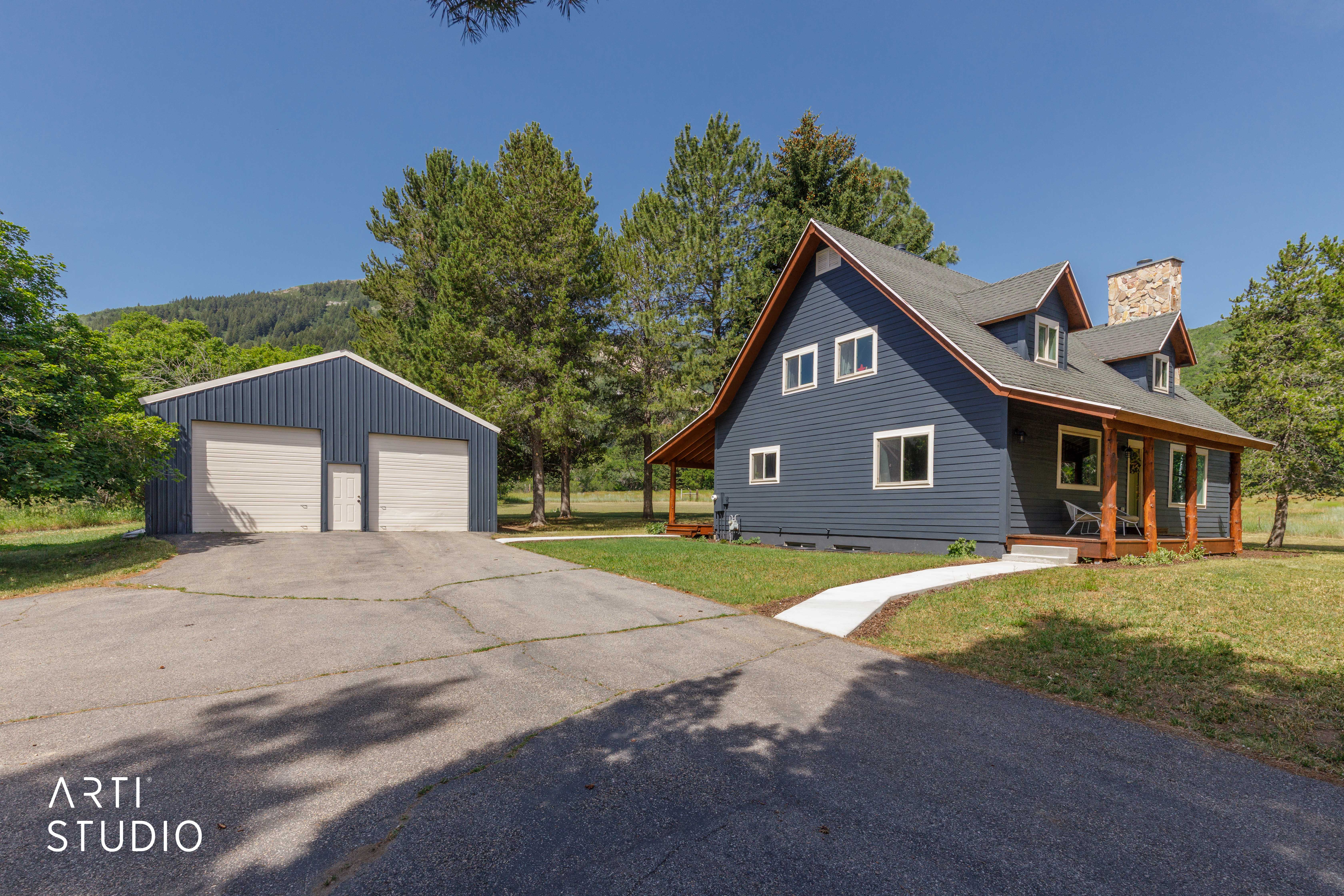 Modern farmhouse-style home with dark blue siding, a stone chimney, and a covered front porch with exposed wood beams