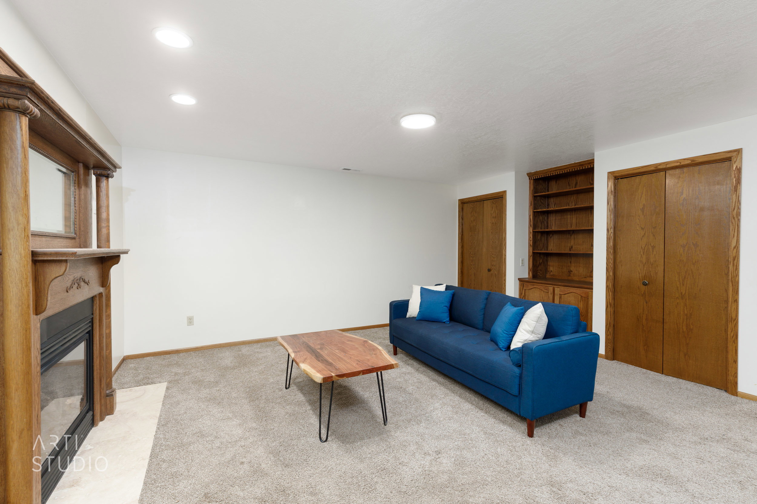Spacious room featuring a wood-mantled fireplace with a light-toned hearth, built-in wooden shelving, and two wooden paneled doors