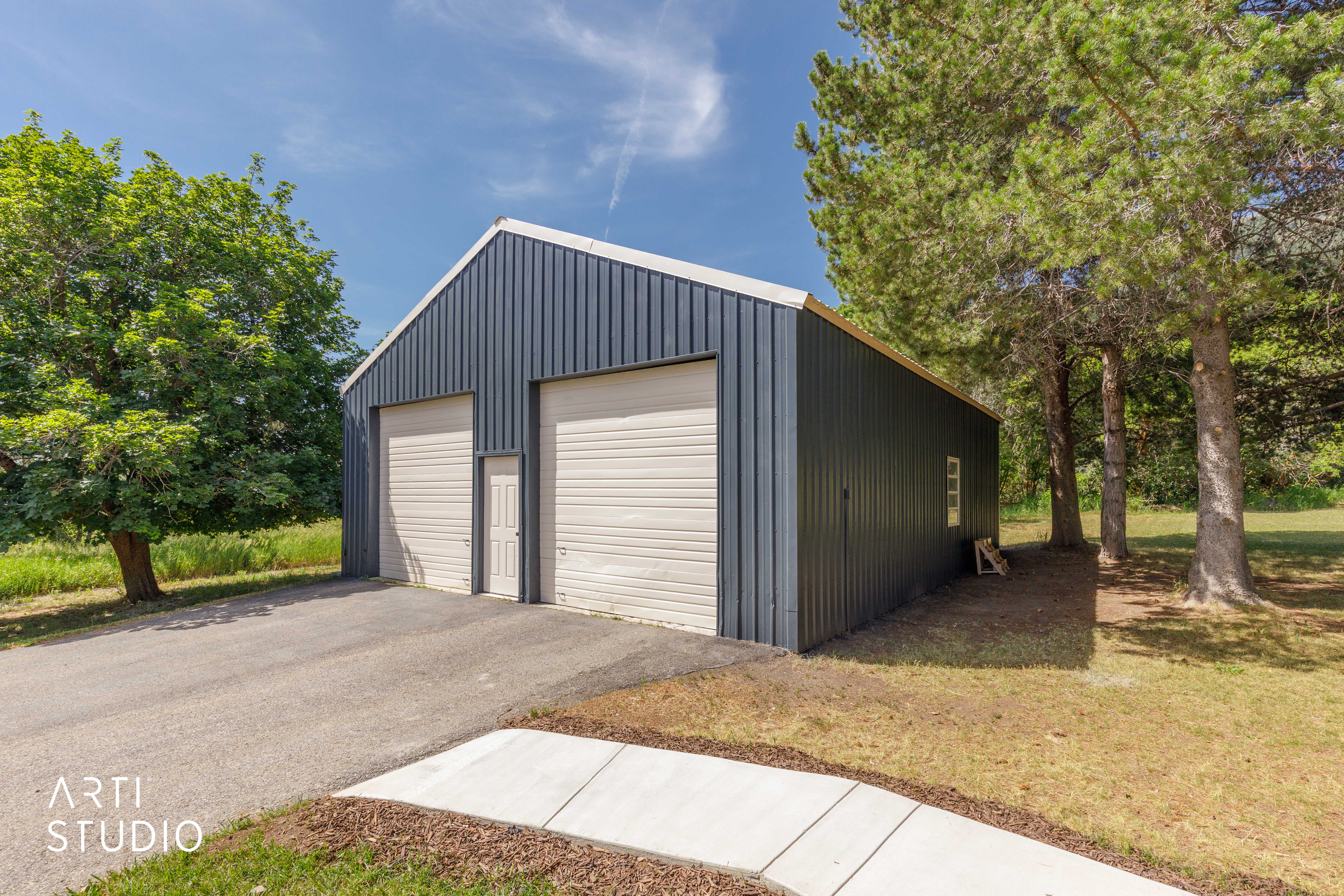 Freestanding outbuilding with two garage doors and a pedestrian entry door, featuring corrugated metal siding and a pitched roof