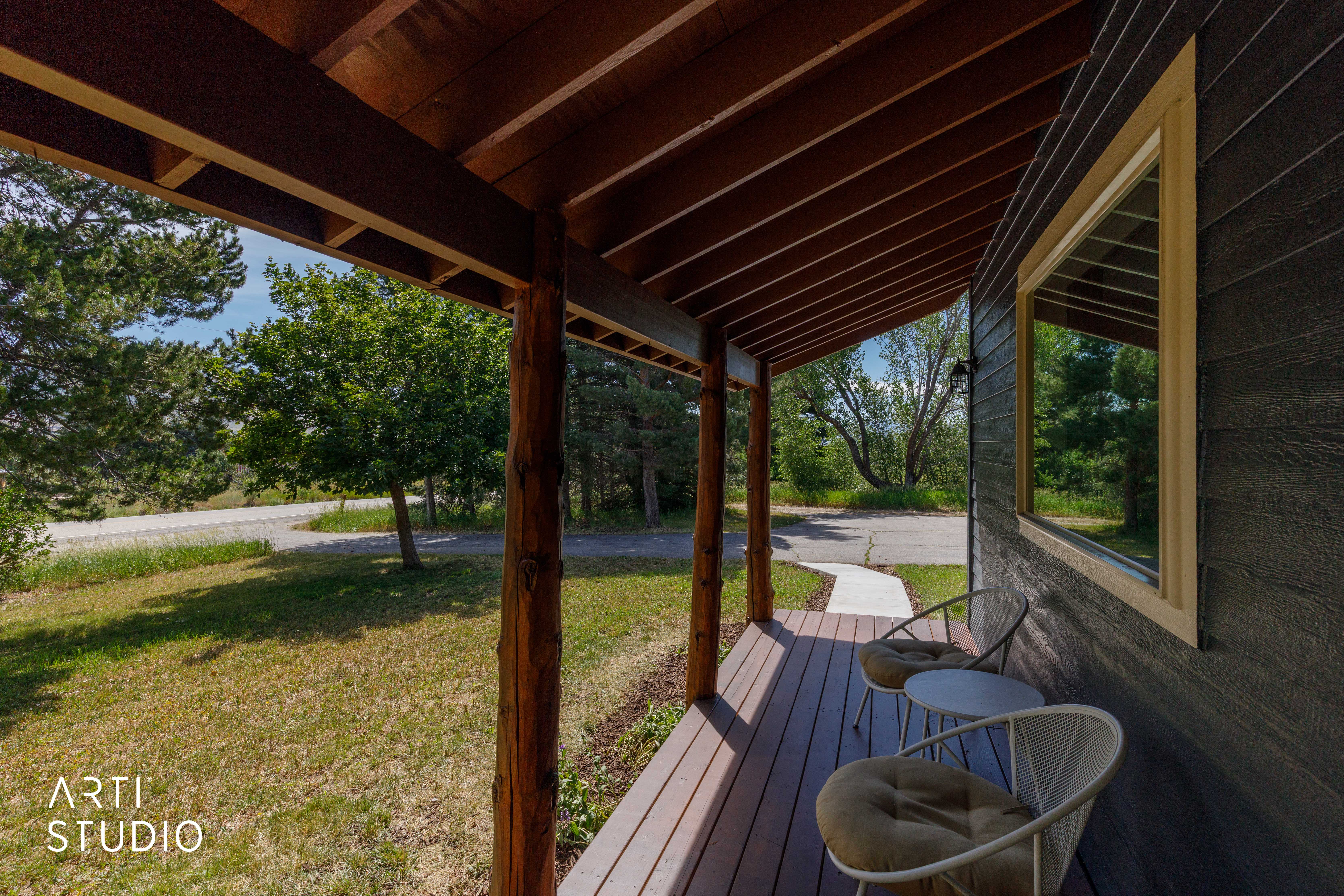 Covered front porch featuring natural wood beams and decking, dark horizontal siding, a light-trimmed window, and a concrete walkway extending to the foreground