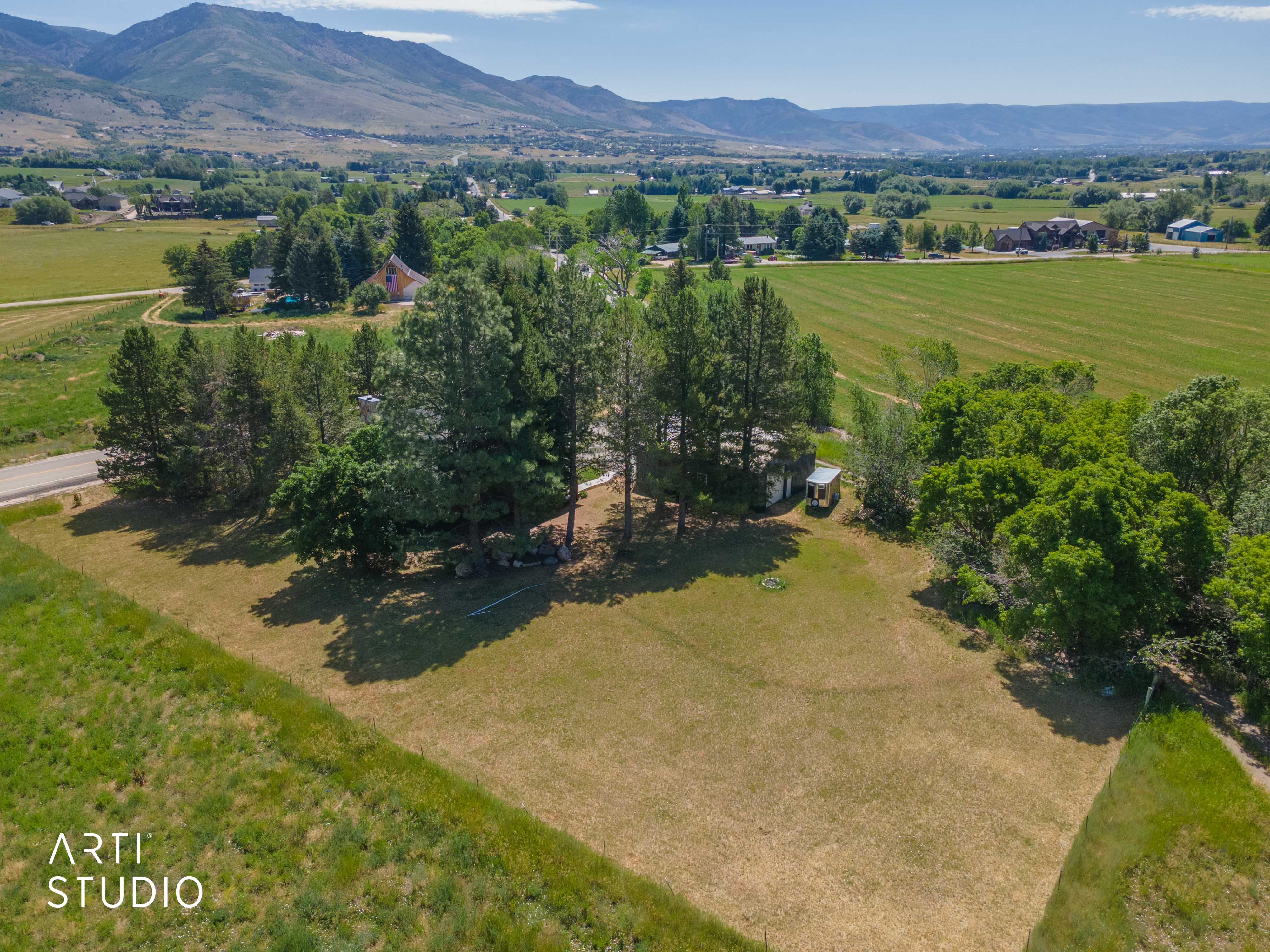 Expansive land parcel featuring mature trees, a clear building site, and distant mountain backdrops