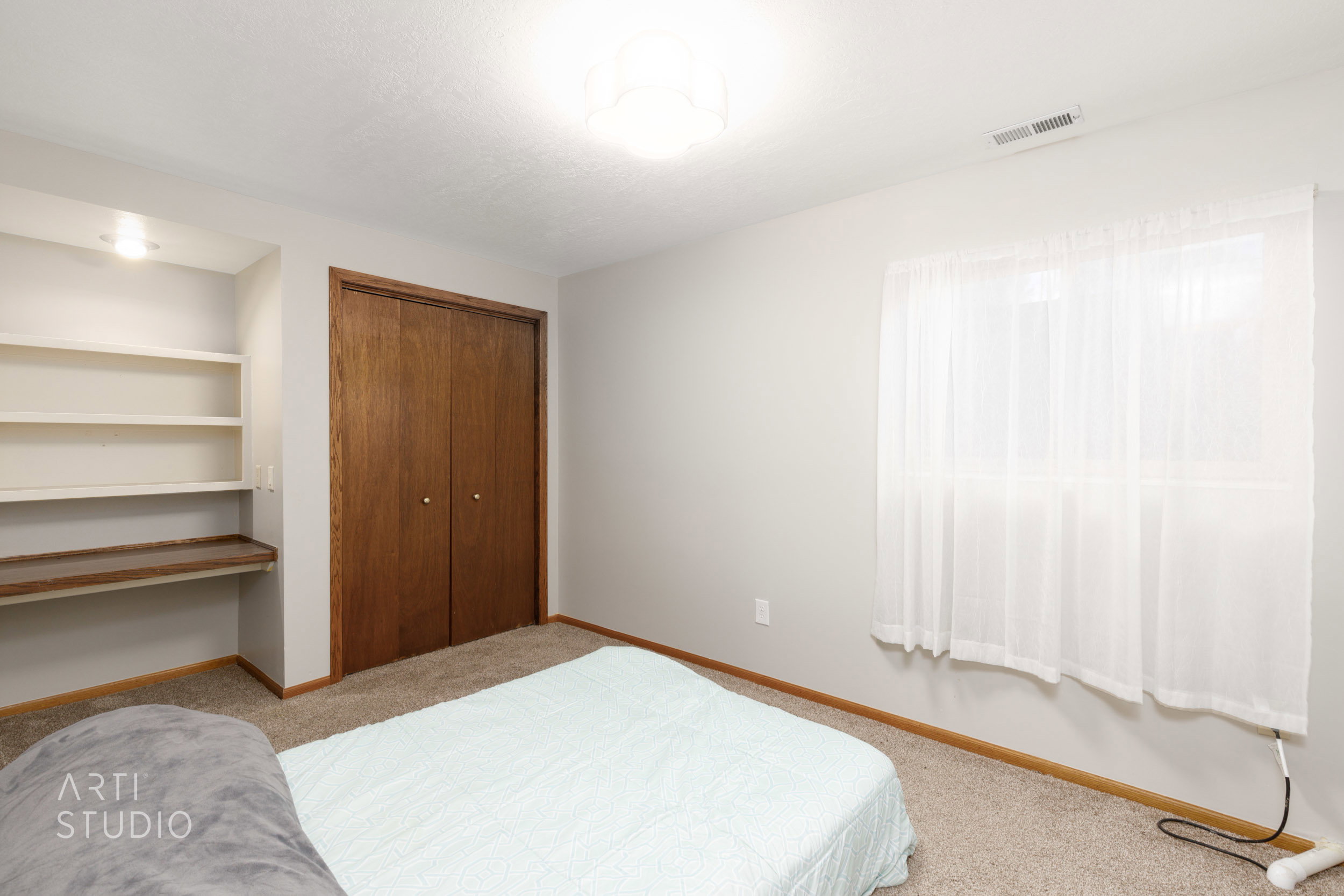 Carpeted room featuring a window with sheer curtains, a built-in shelving unit with a wood-finish countertop, and a double-door closet