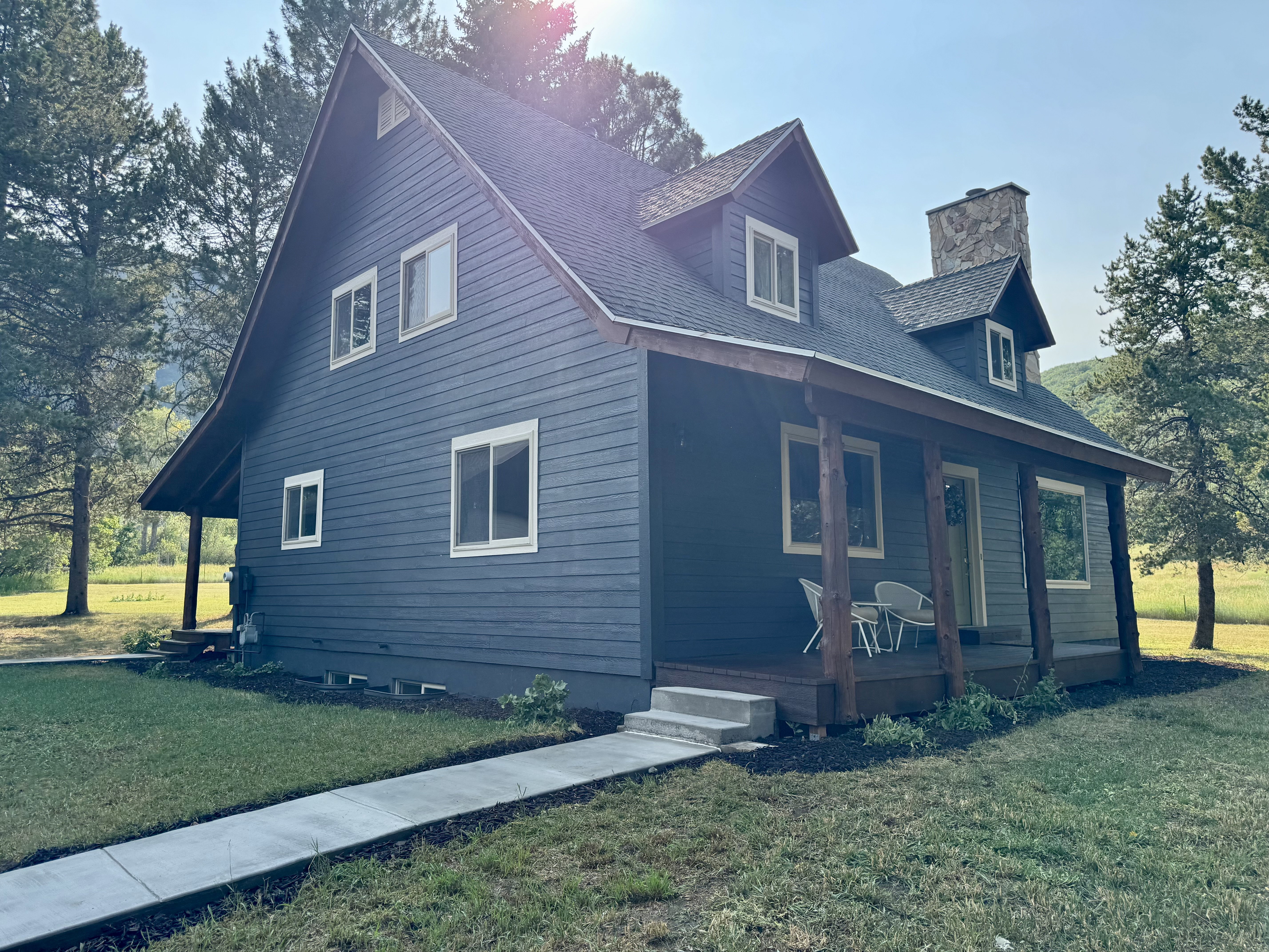 A-frame style residence featuring dark blue siding, a covered porch with natural wood posts, and a prominent stone chimney