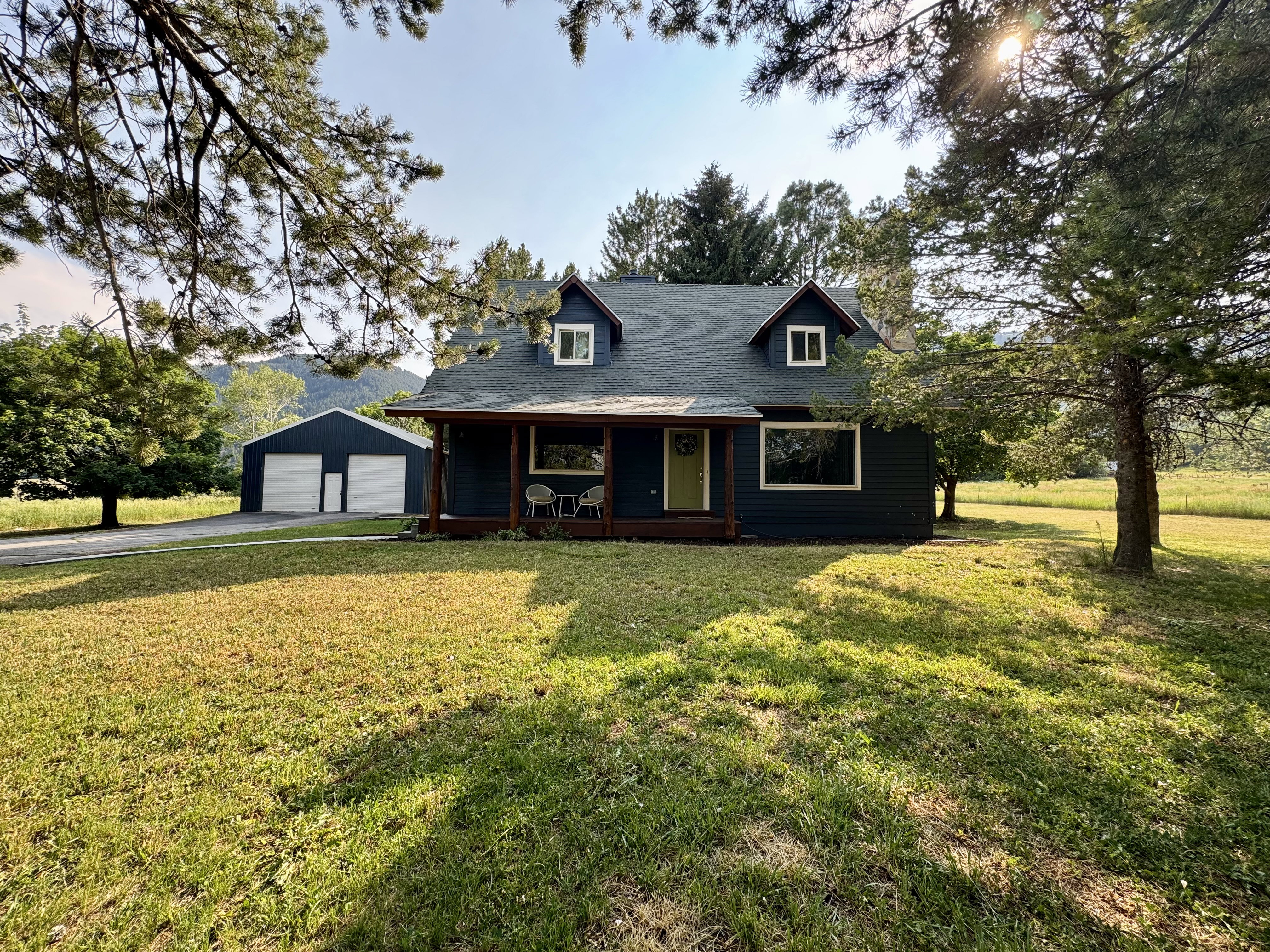 Two-story residence featuring a dark blue exterior siding, dormer windows, and a covered front porch