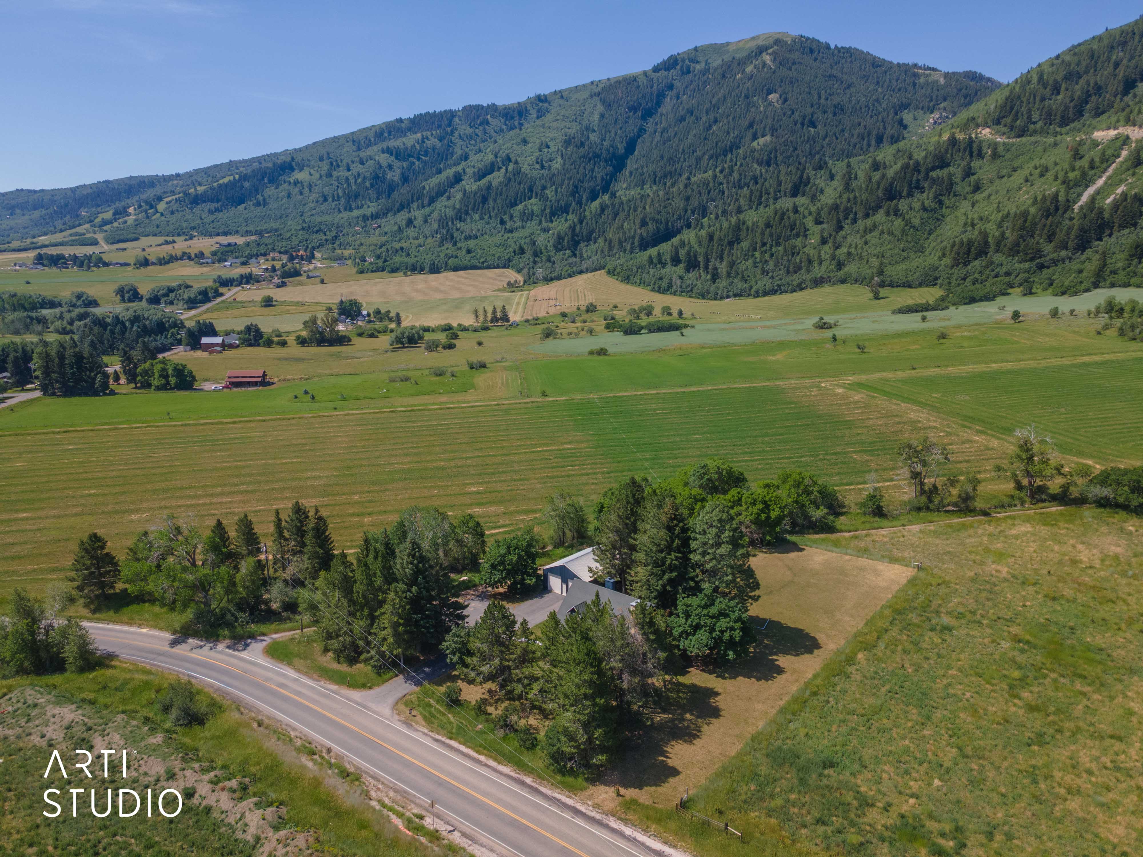 Aerial perspective showcasing a property surrounded by expansive green fields and mature trees, with a mountainous backdrop