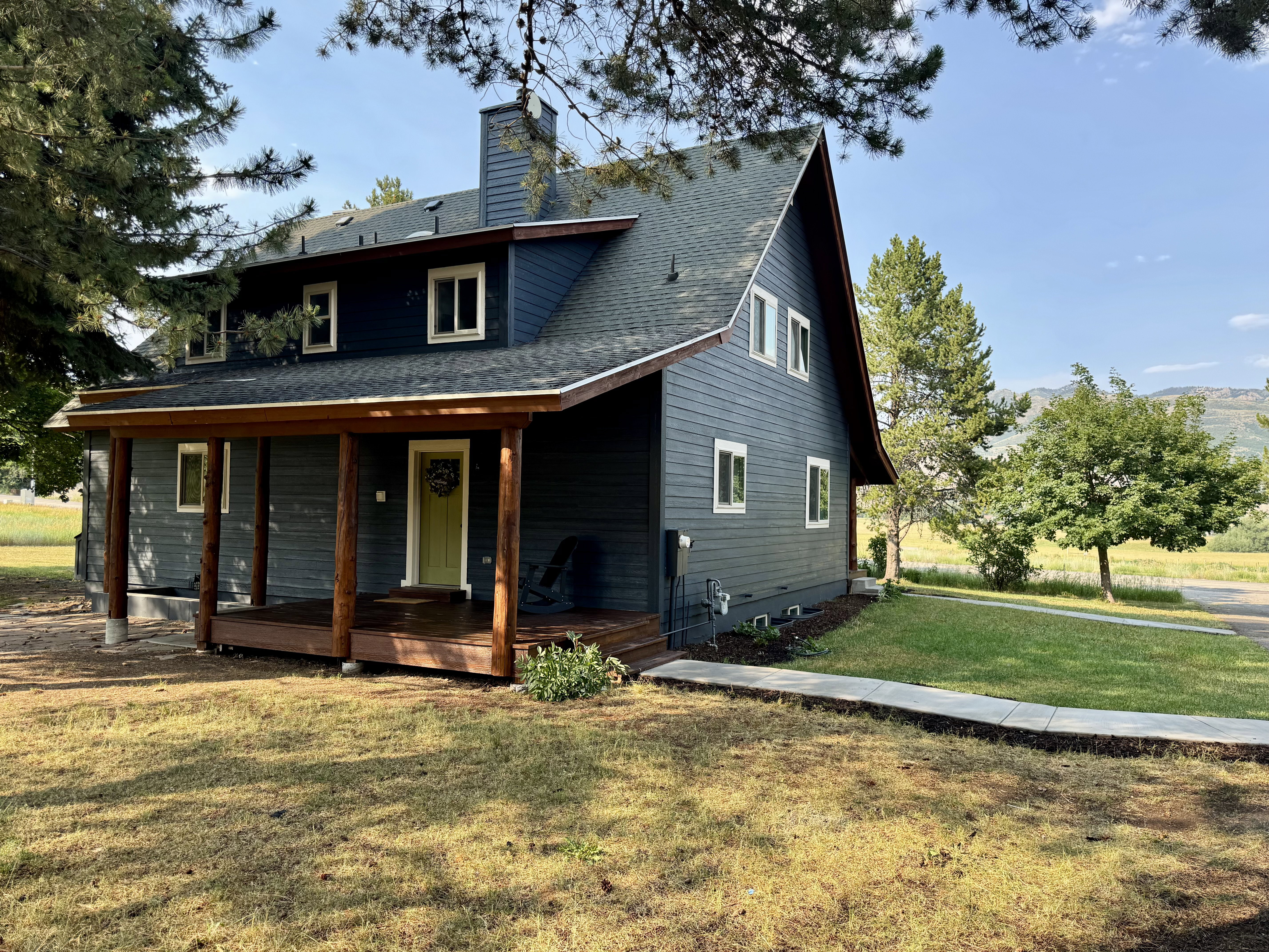 Two-story residence featuring dark siding, a covered front porch with natural wood posts, and a prominent chimney