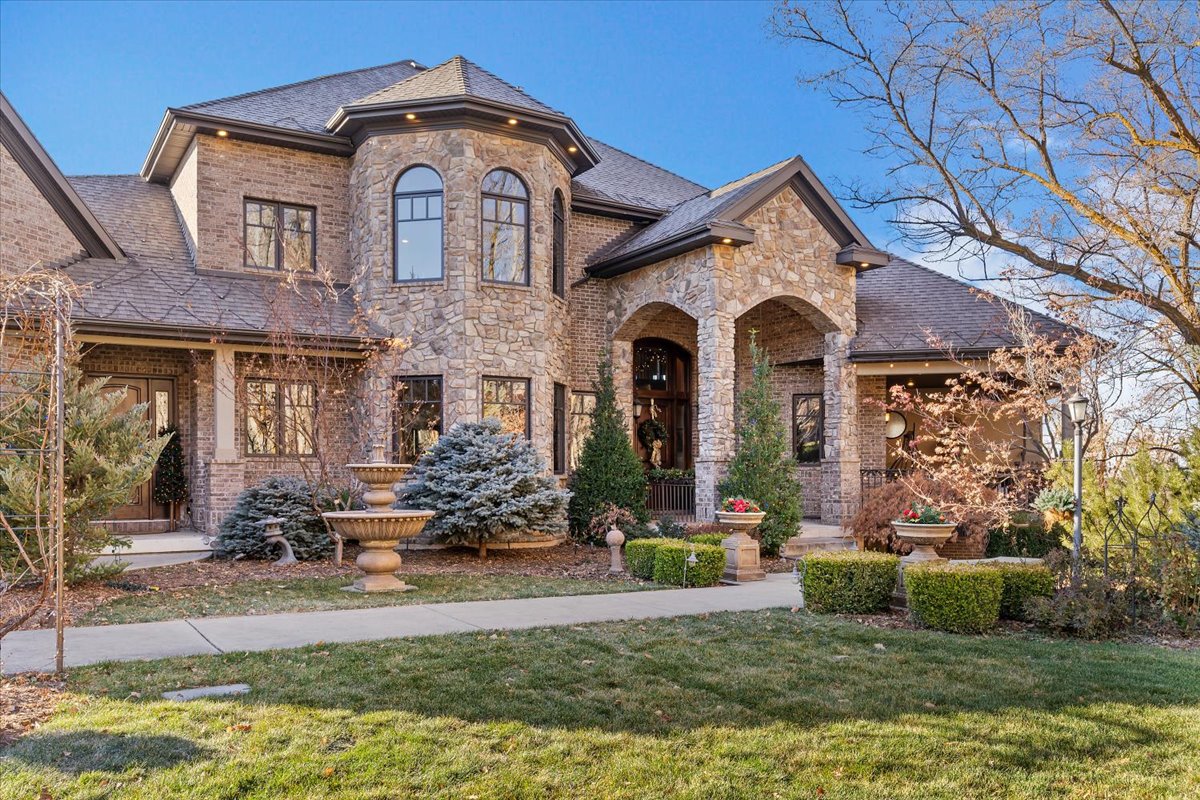 Stately stone and brick facade featuring an arched entry, a turret, multiple windows, and a manicured lawn