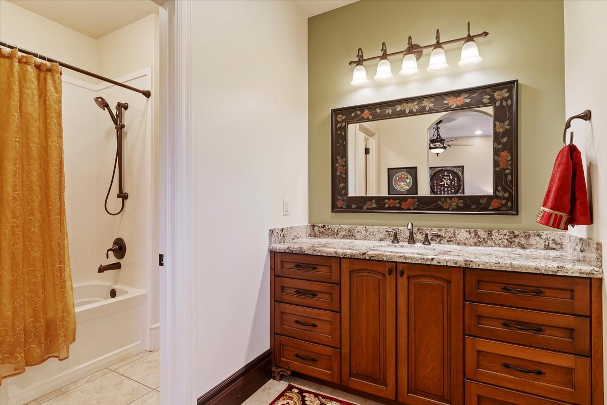 Bathroom featuring a wood-finish vanity with granite-style countertop, a decorative framed mirror, and a five-light vanity fixture